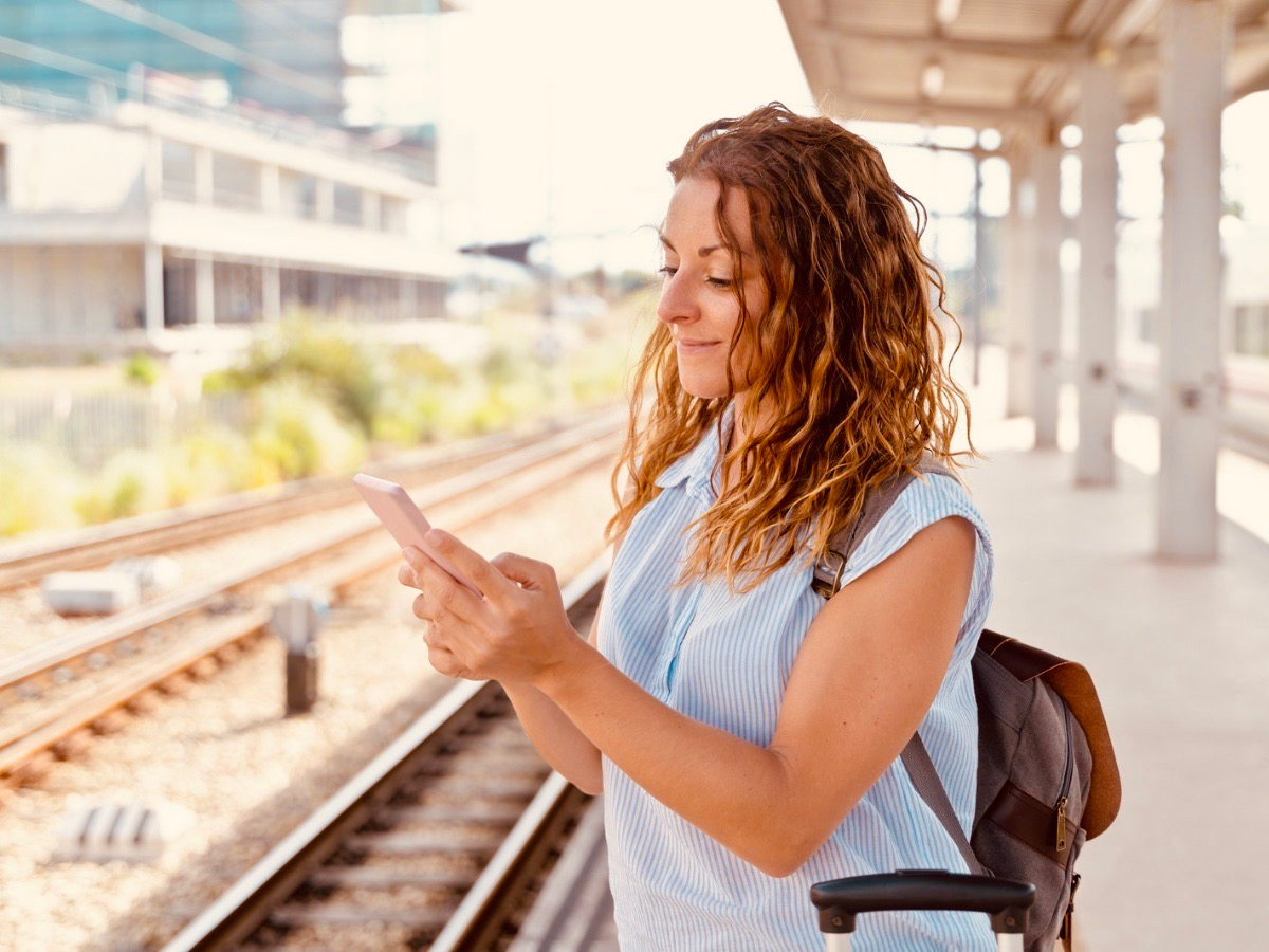 A woman with a backpack and luggage checking her phone while waiting at a train platform