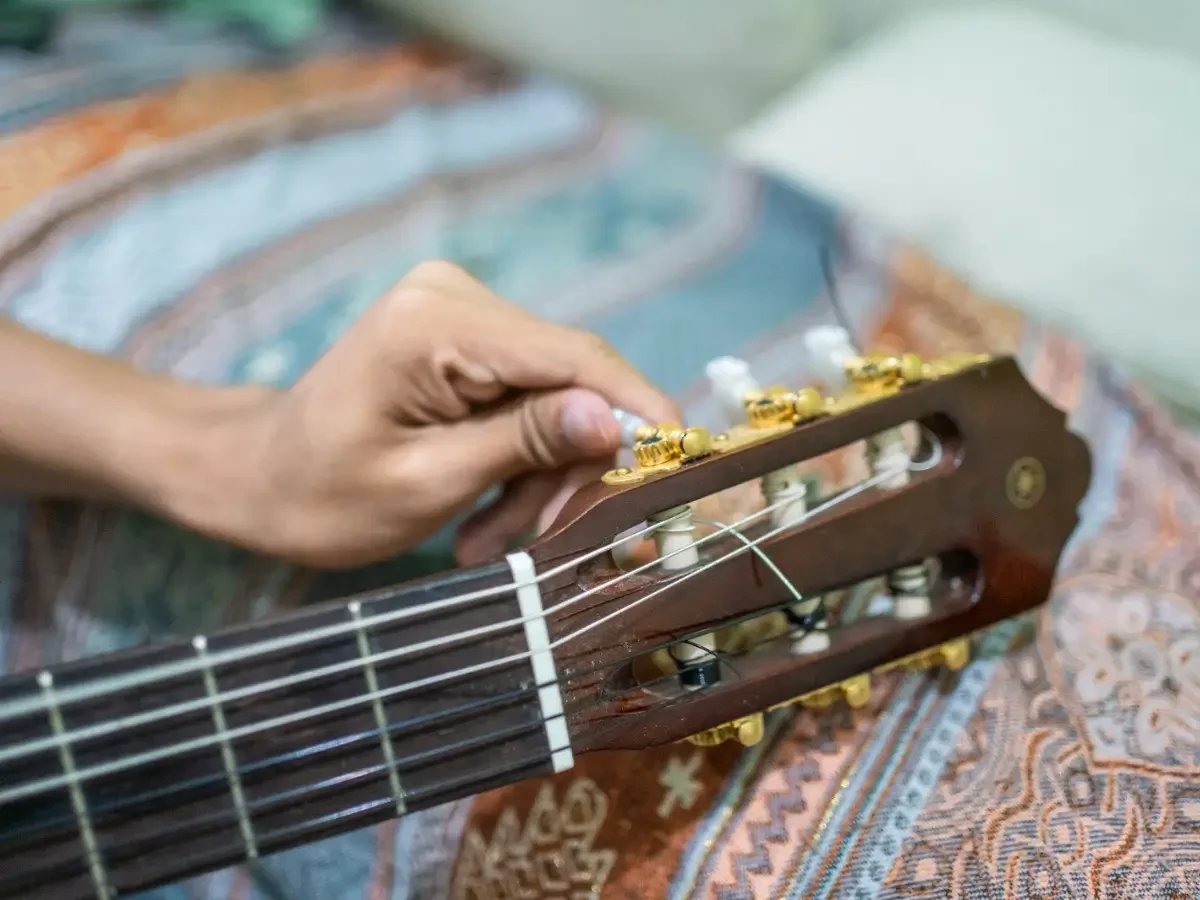 A hand turning a guitar tuning peg, adjusting the instrument before playing.