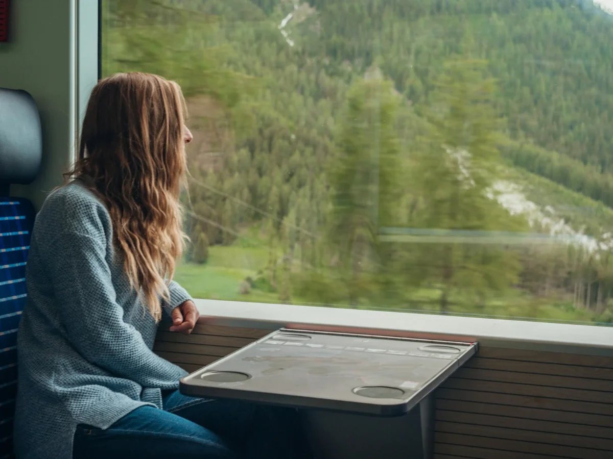 A woman gazing out a train window at a blurred green landscape, representing a life still in formation