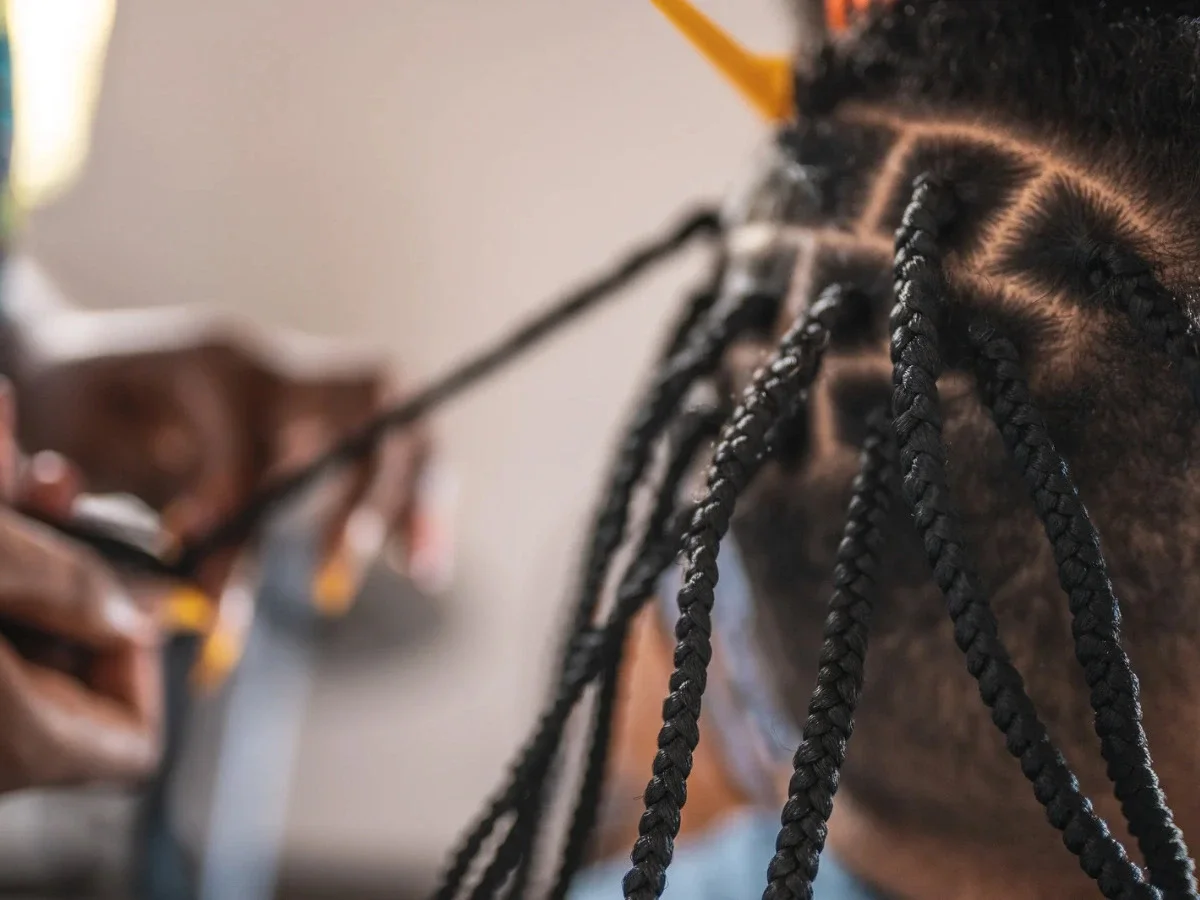 Close-up of a braider's hands installing box braids, capturing the technique and precision behind a generations-old Black hair tradition
