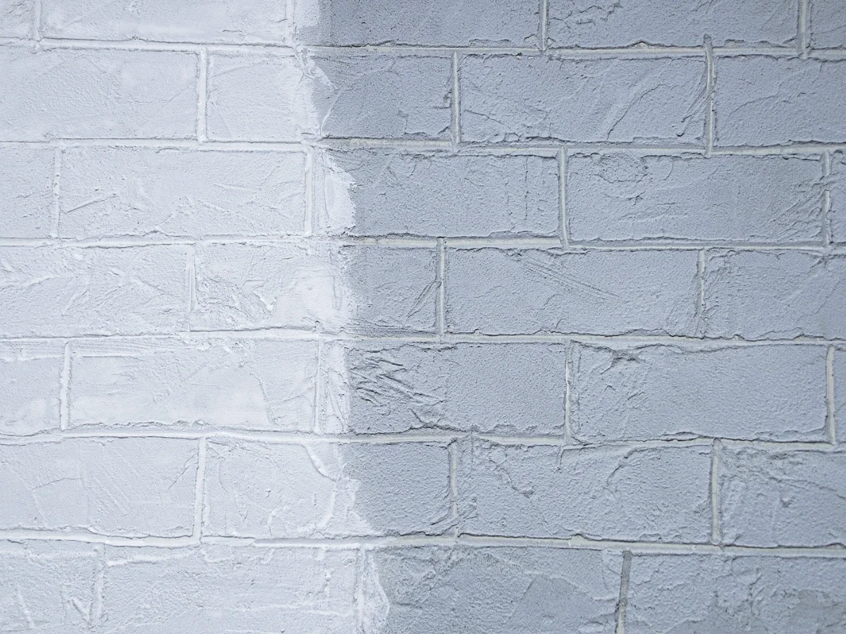 A brick wall half-painted, one side old and one side new, representing the labor of leaving something behind