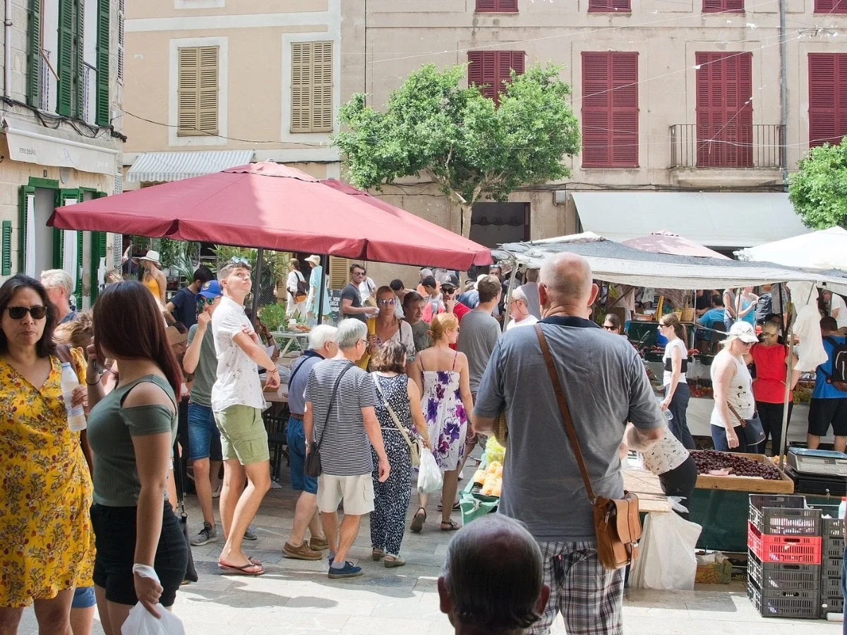 A crowded outdoor market plaza filled with shoppers and vendors under red umbrellas