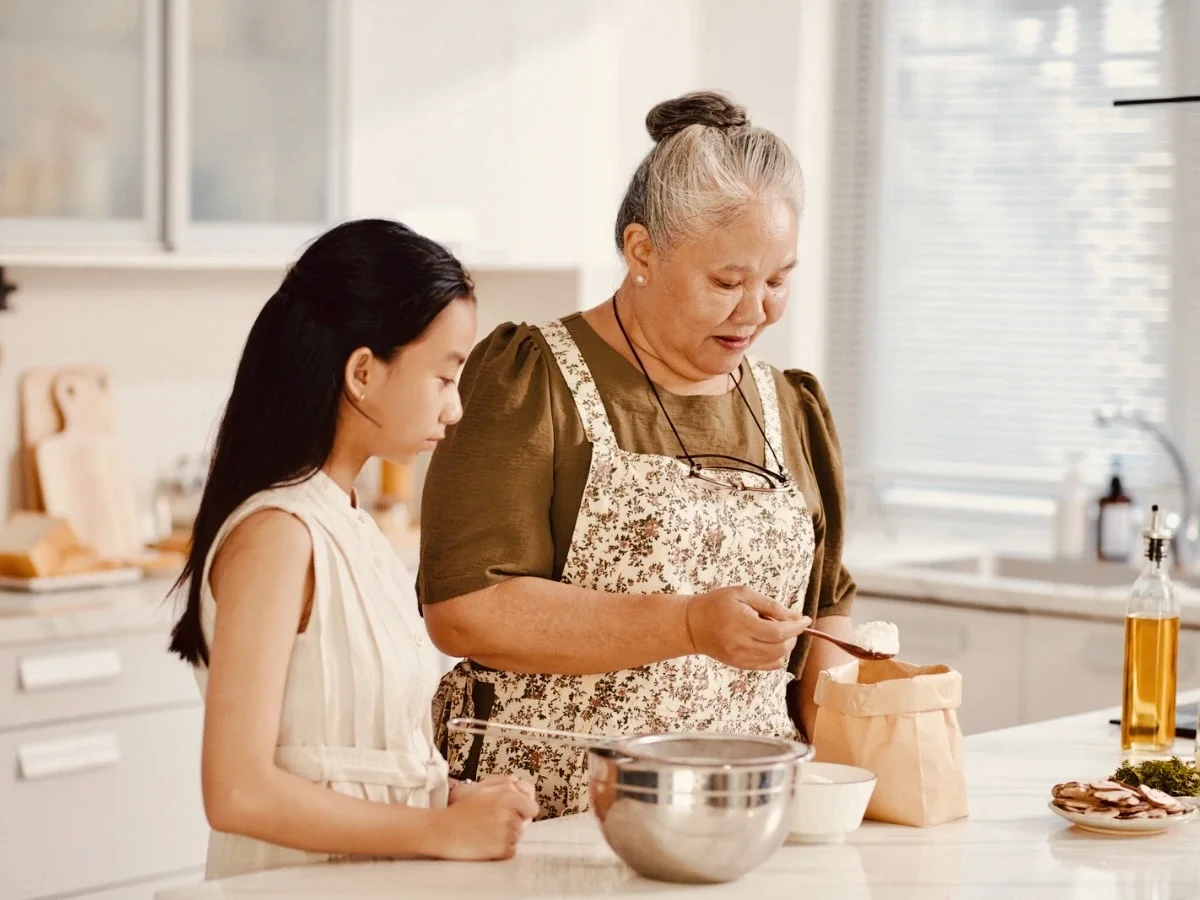Grandmother and granddaughter baking together, passing down a family recipe through hands-on teaching