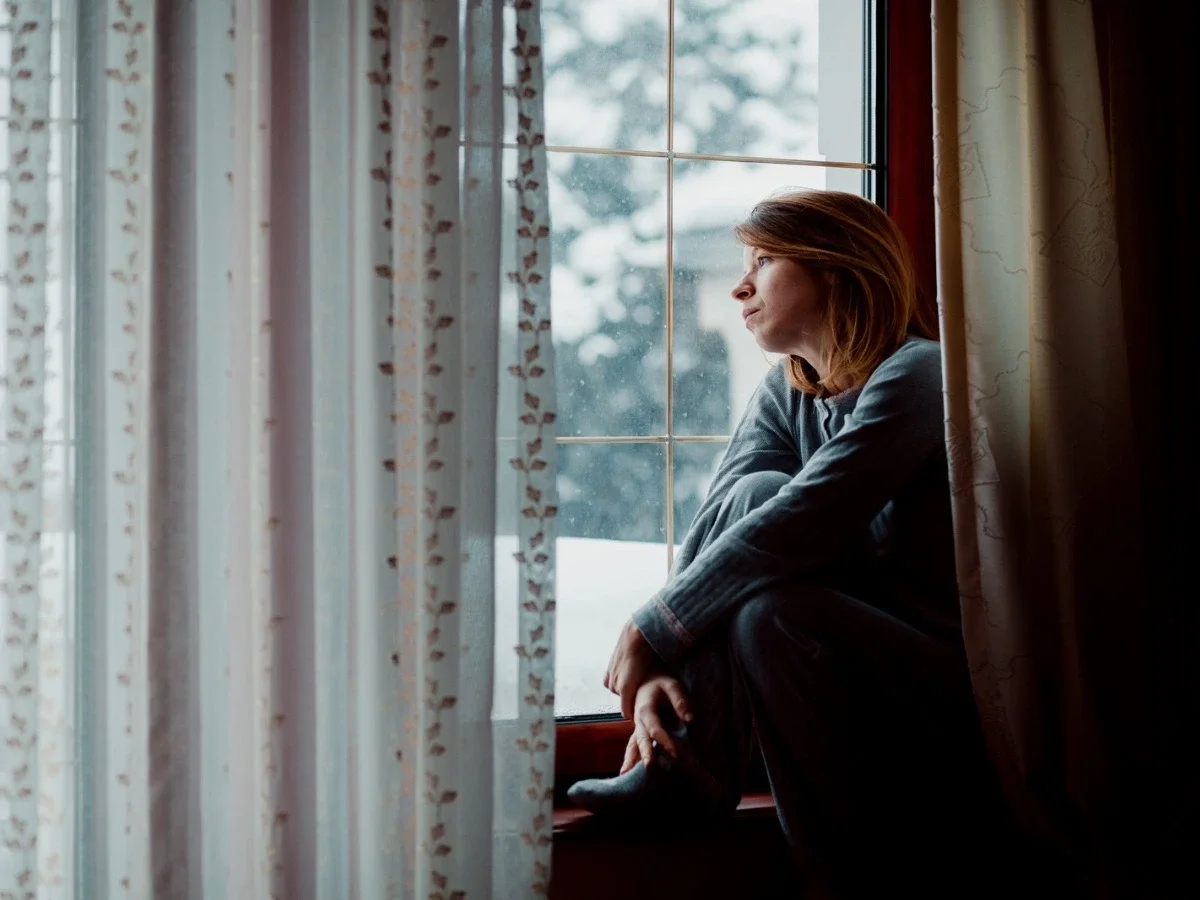 Woman sitting by a window looking outside in quiet contemplation