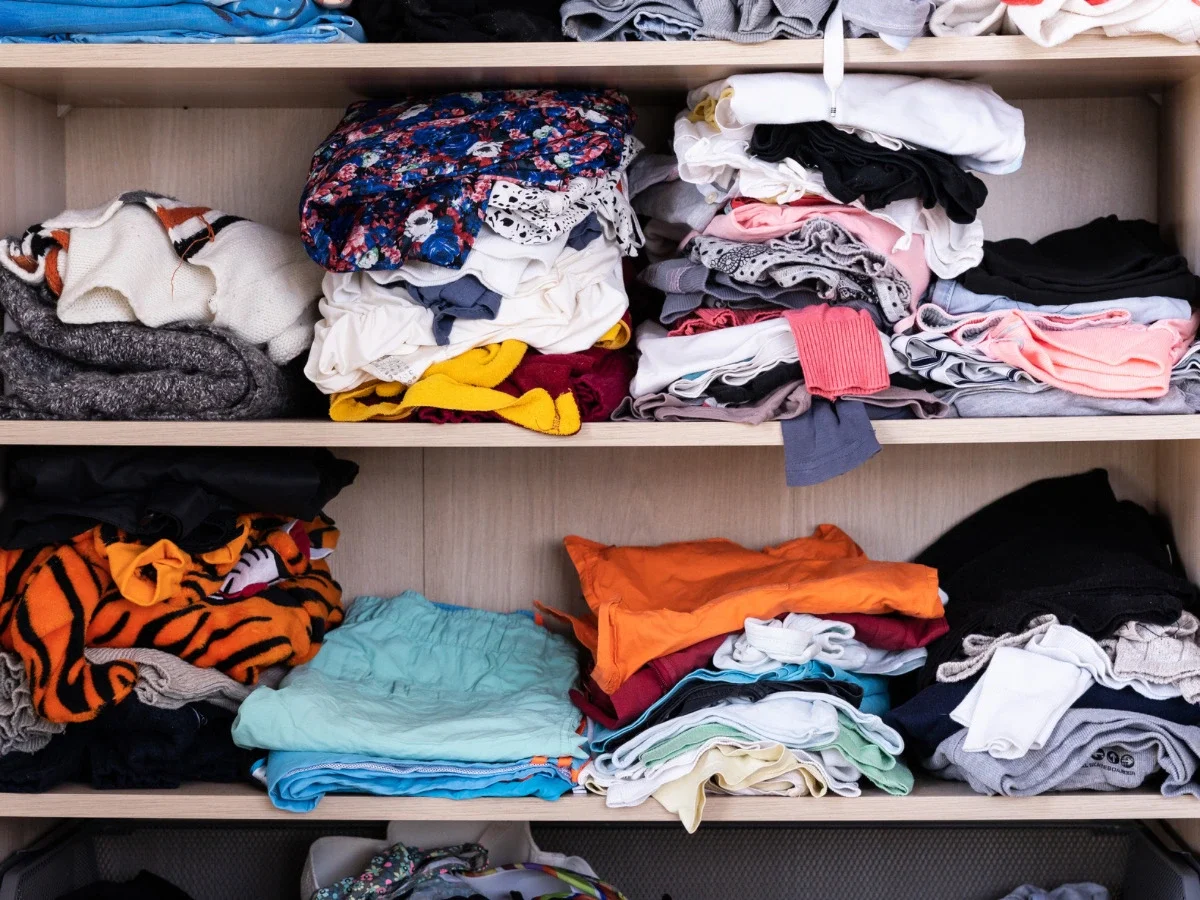 Overflowing closet shelves stacked with folded and disorganized clothing