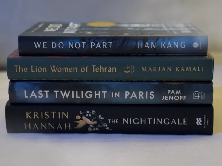 A stack of favorite books read in 2025 featuring emotionally powerful and beautifully written novels such as The Nightingale, We Do Not Part, Last Twilight in Paris, and The Lion Women of Tehran, highlighting personal reading superlatives.