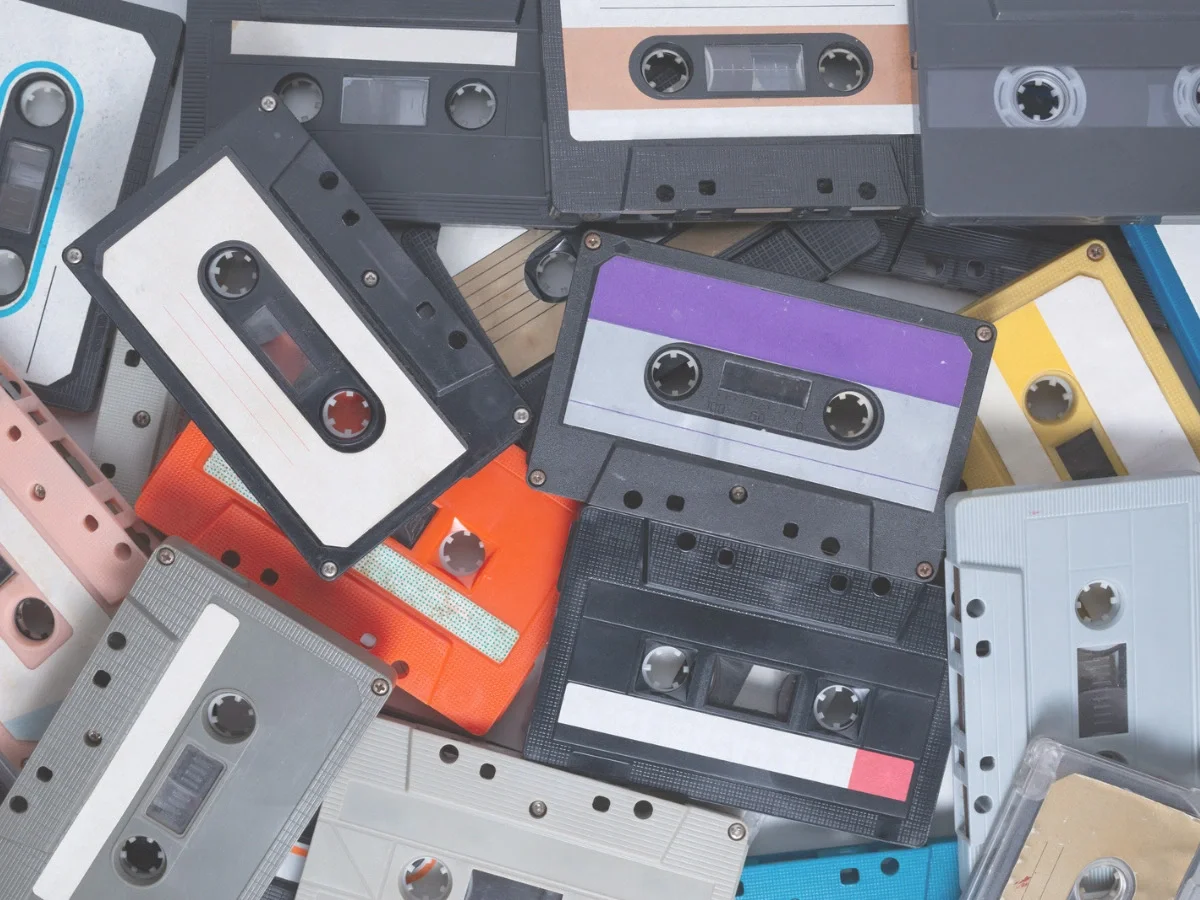 An overhead view of a loose pile of colorful, worn cassette tapes in varied designs—accompanying "Why the Object Keeps Coming Back," on the return of physical music in She The King's essay.
