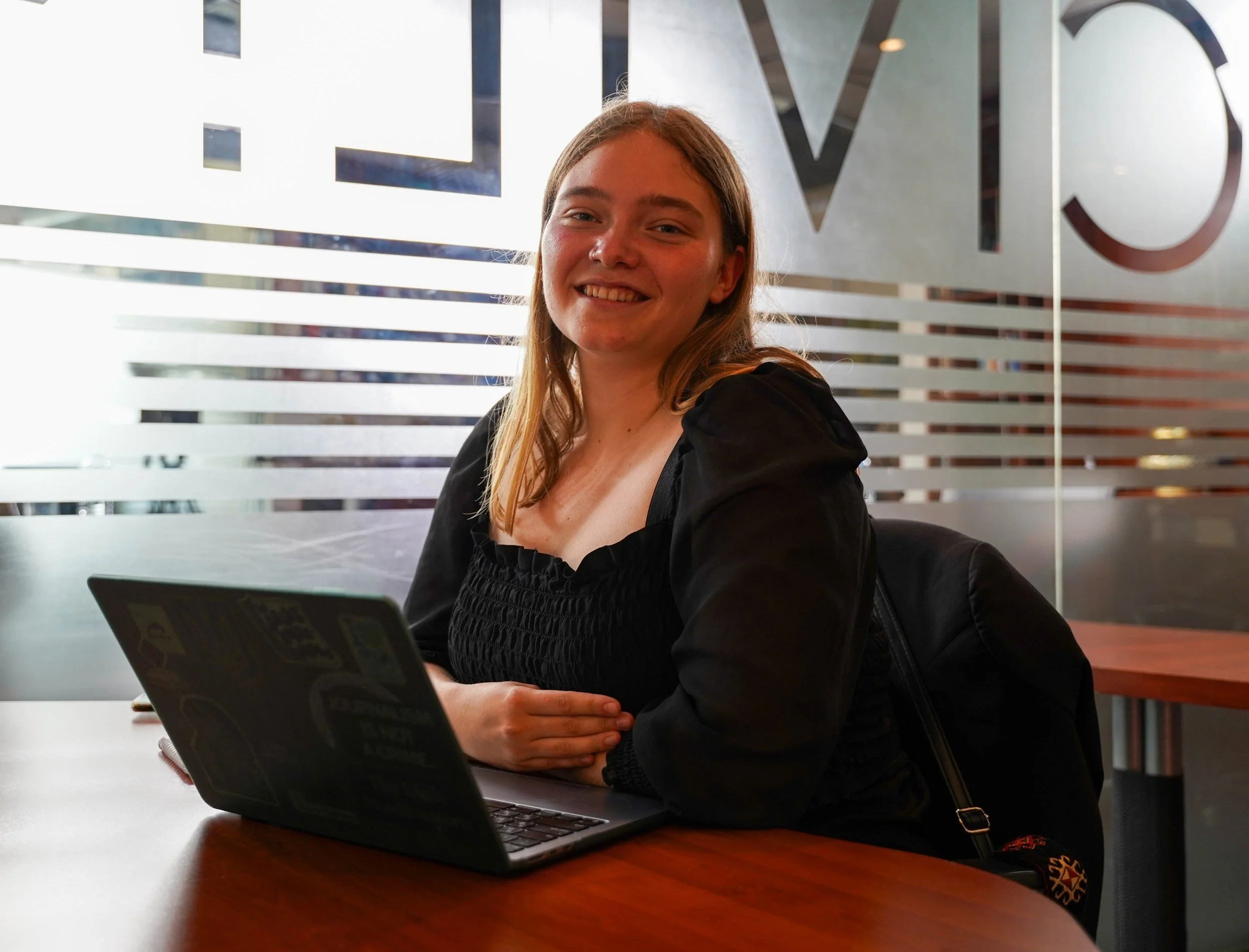 Young Woman at an office, smiling and seated in front of a laptop