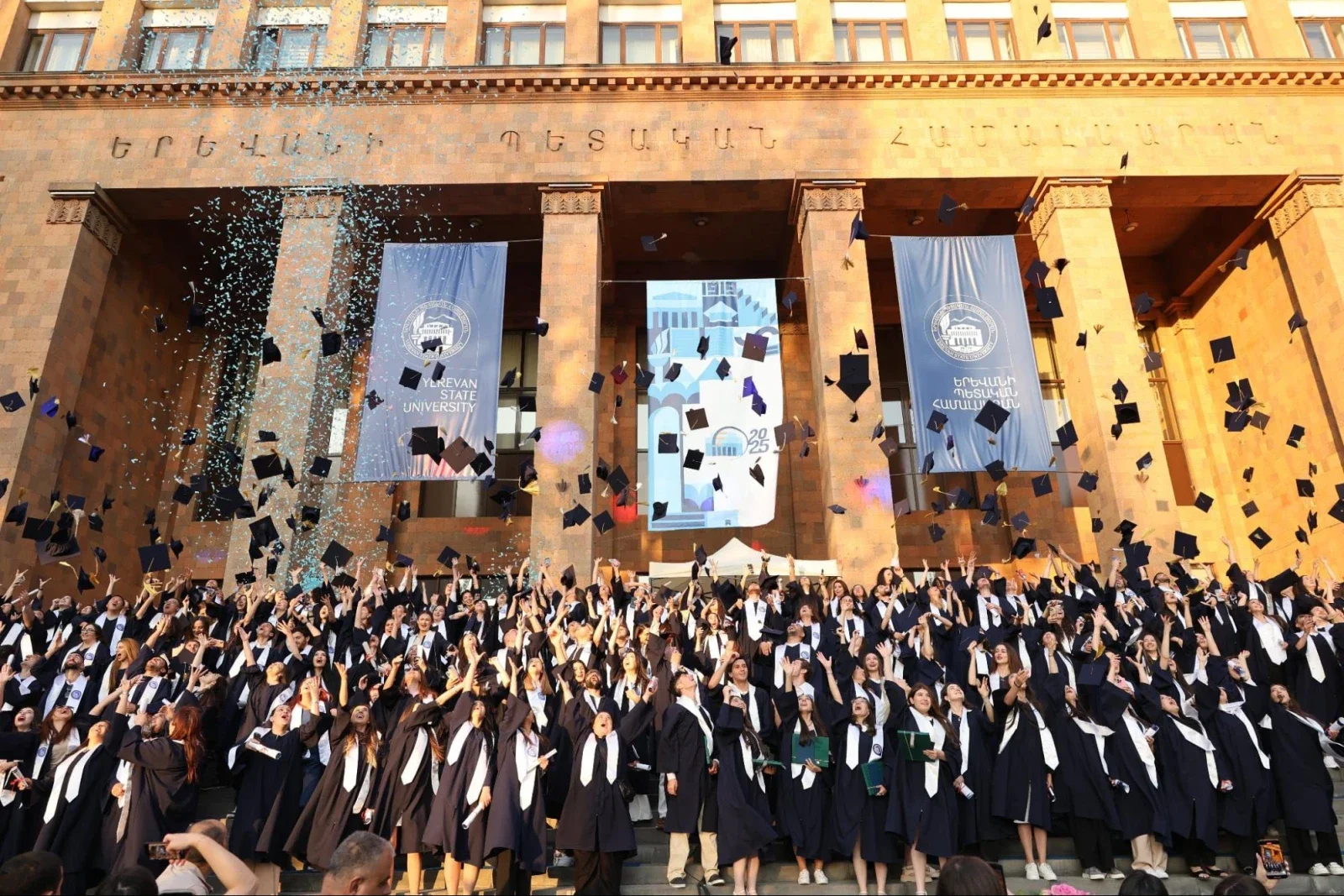 Yerevan State University graduates toss their caps in the air.