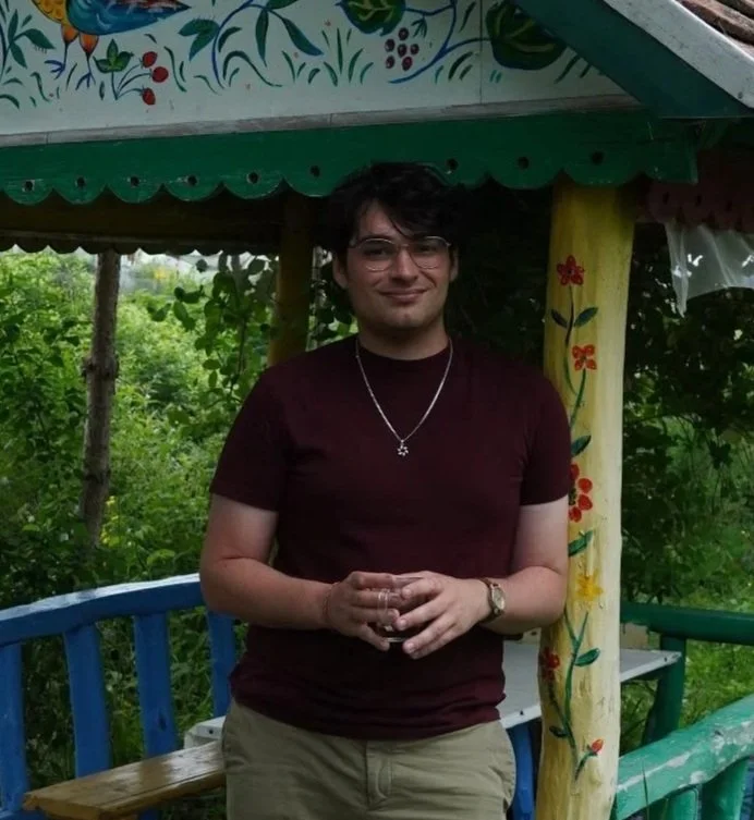 A bot standing, smiling softly, with a cup in his hands.