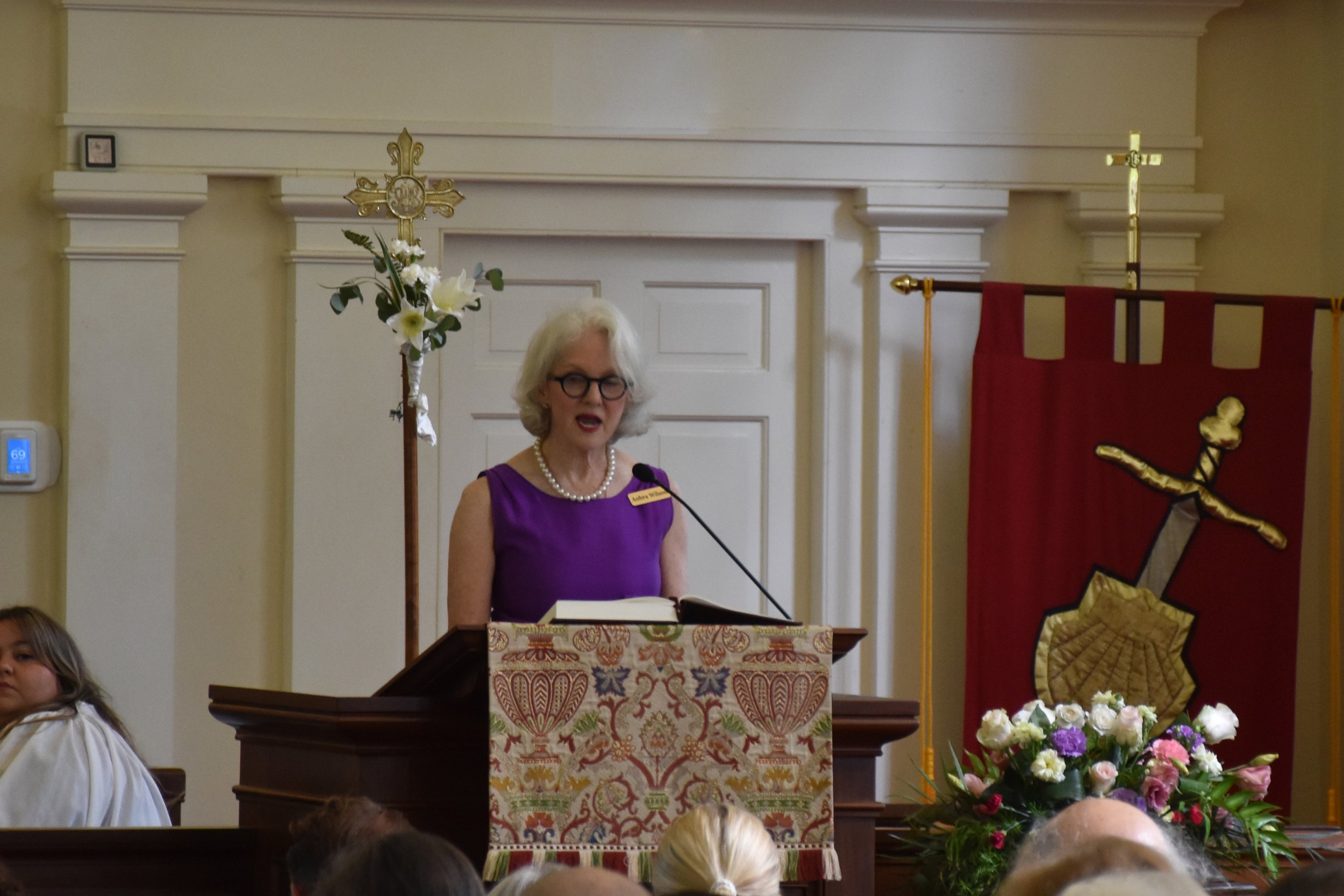 woman in purple dress reading from podium at church - lector charleston, SC