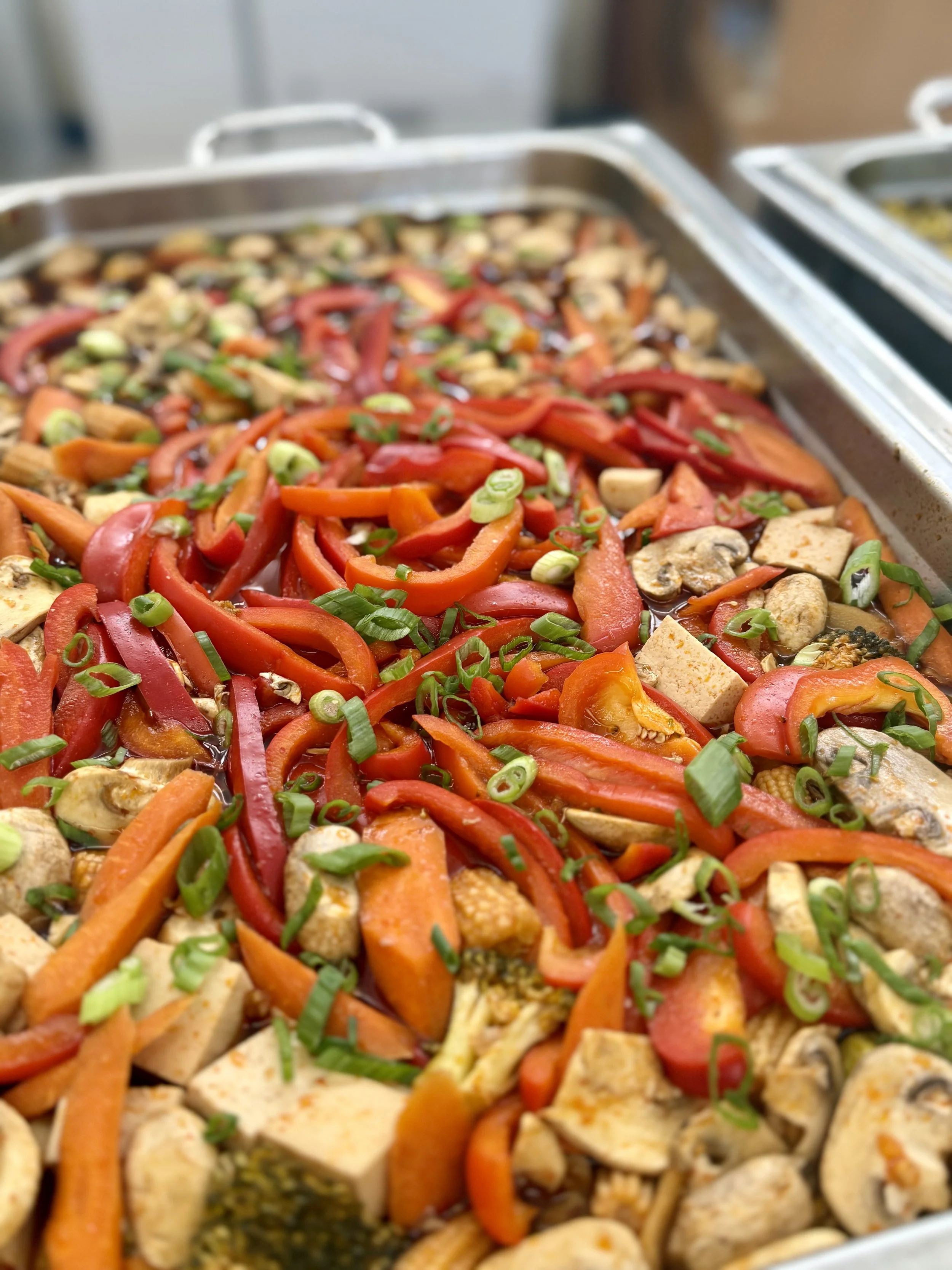 Tray of cooked vegetables including sliced red and orange bell peppers, mushrooms, and chopped green onions.