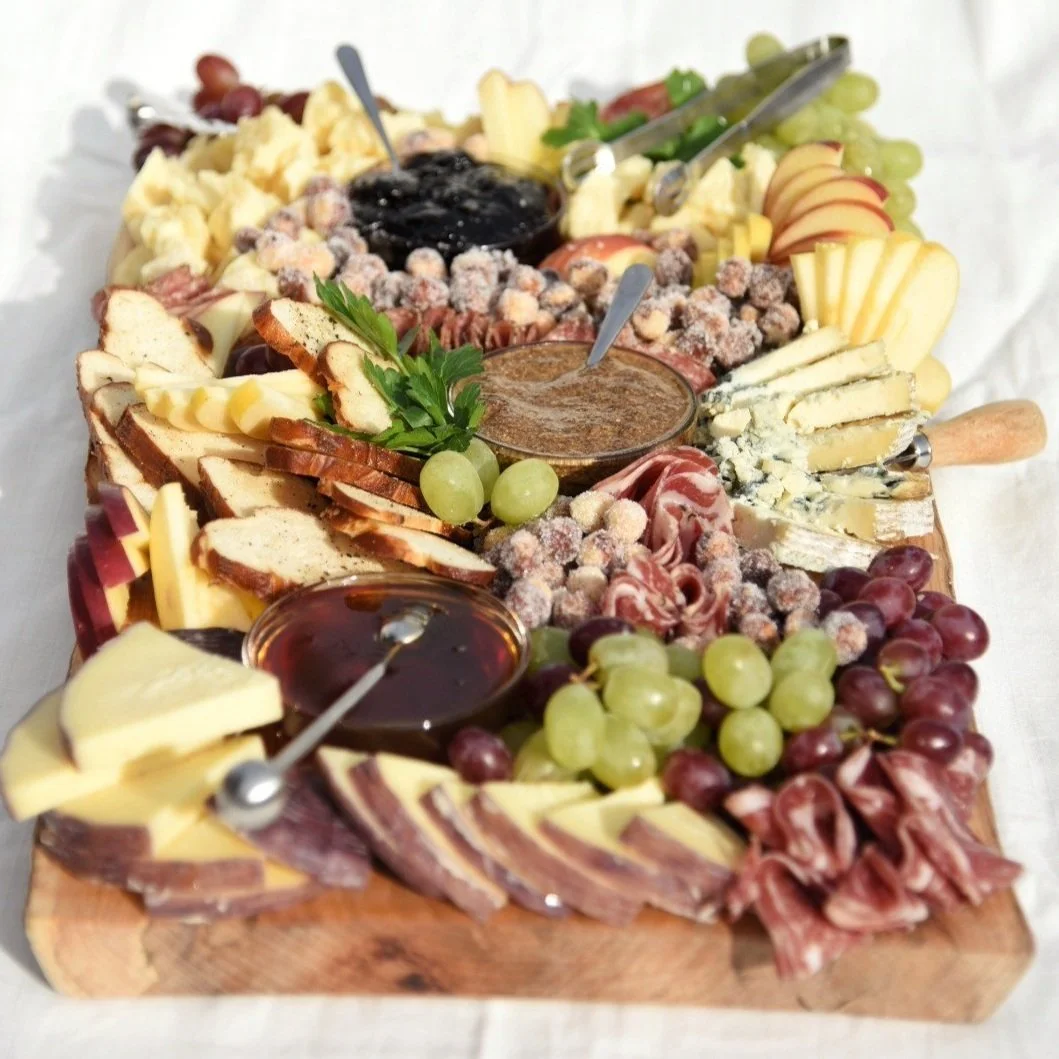 Charcuterie board with cheeses, grapes, sliced meats, bread, and dipping sauces.