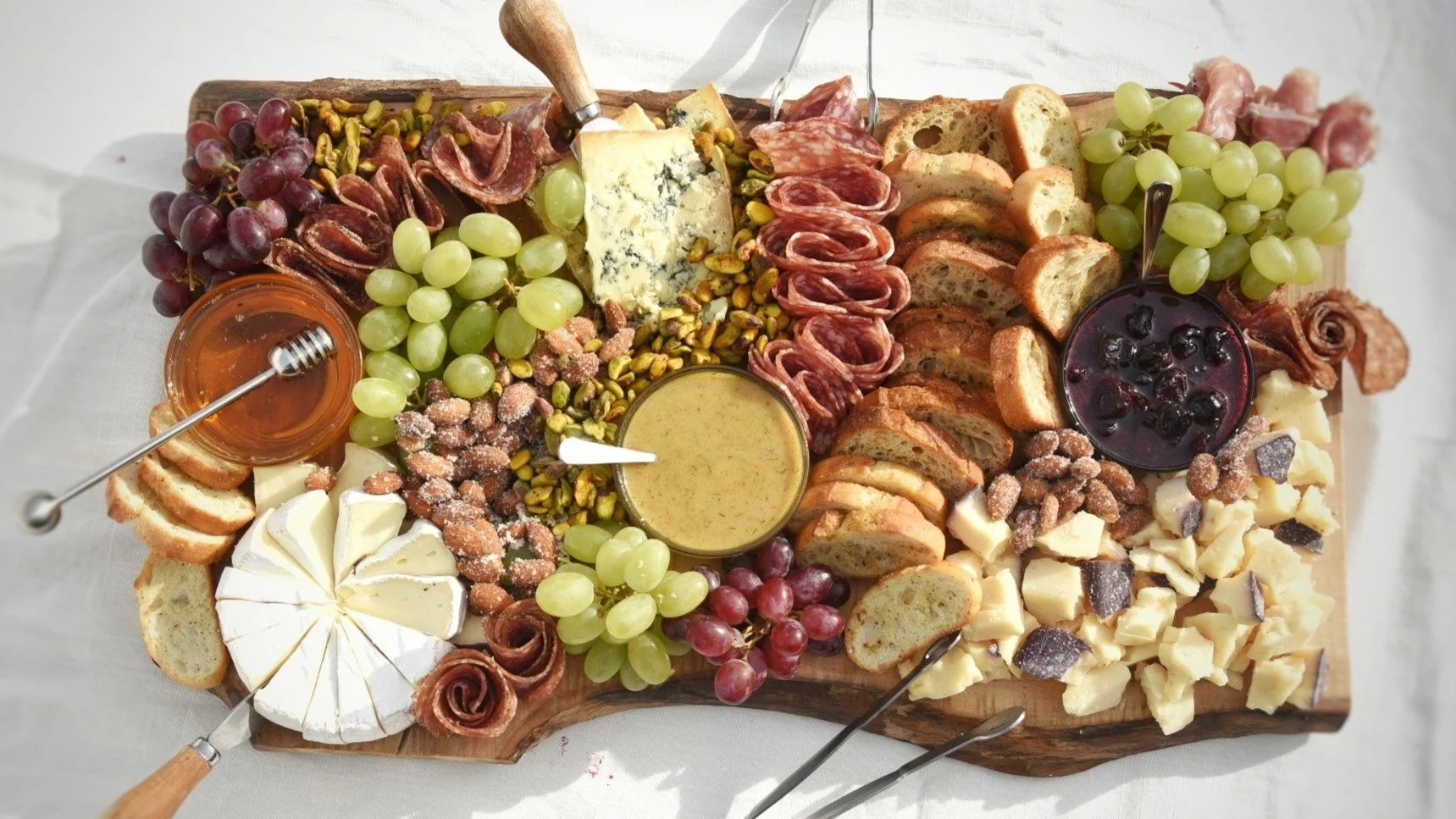 A cheese and charcuterie board with grapes, honey, and crackers.