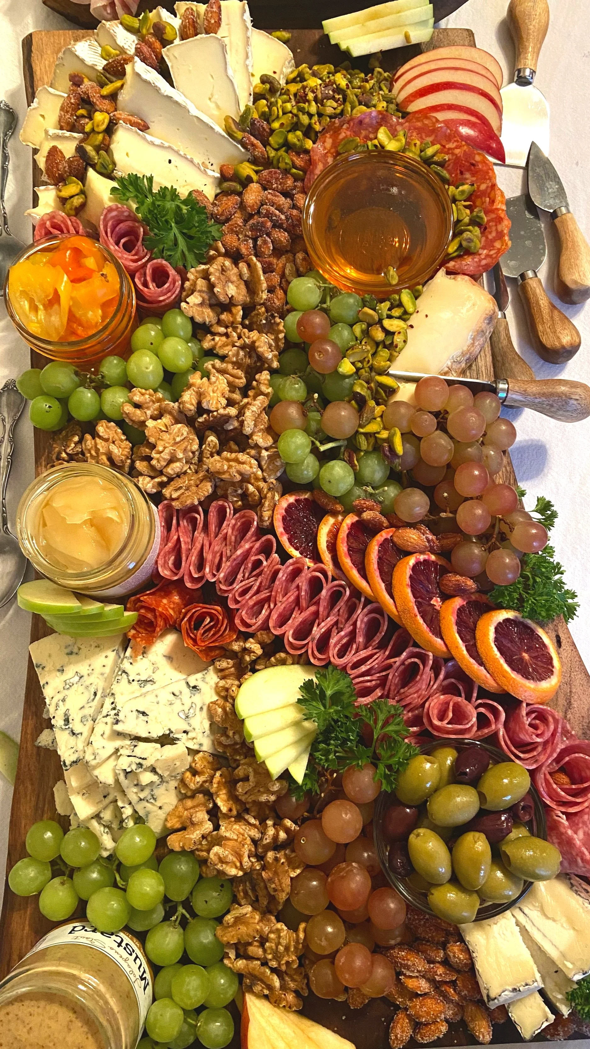 A cheese and charcuterie board with various cheeses, grapes, nuts, fruits, meats, and condiments.