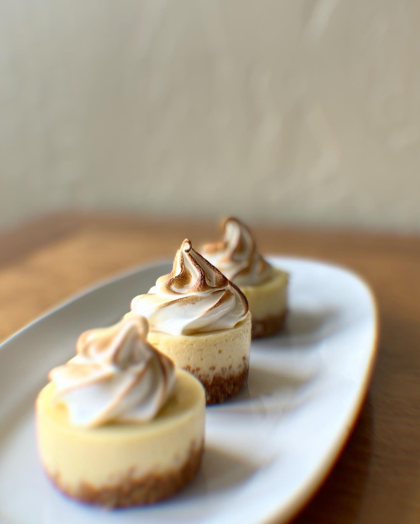 Three cheesecakes topped with whipped cream and chocolate swirls on a white platter.