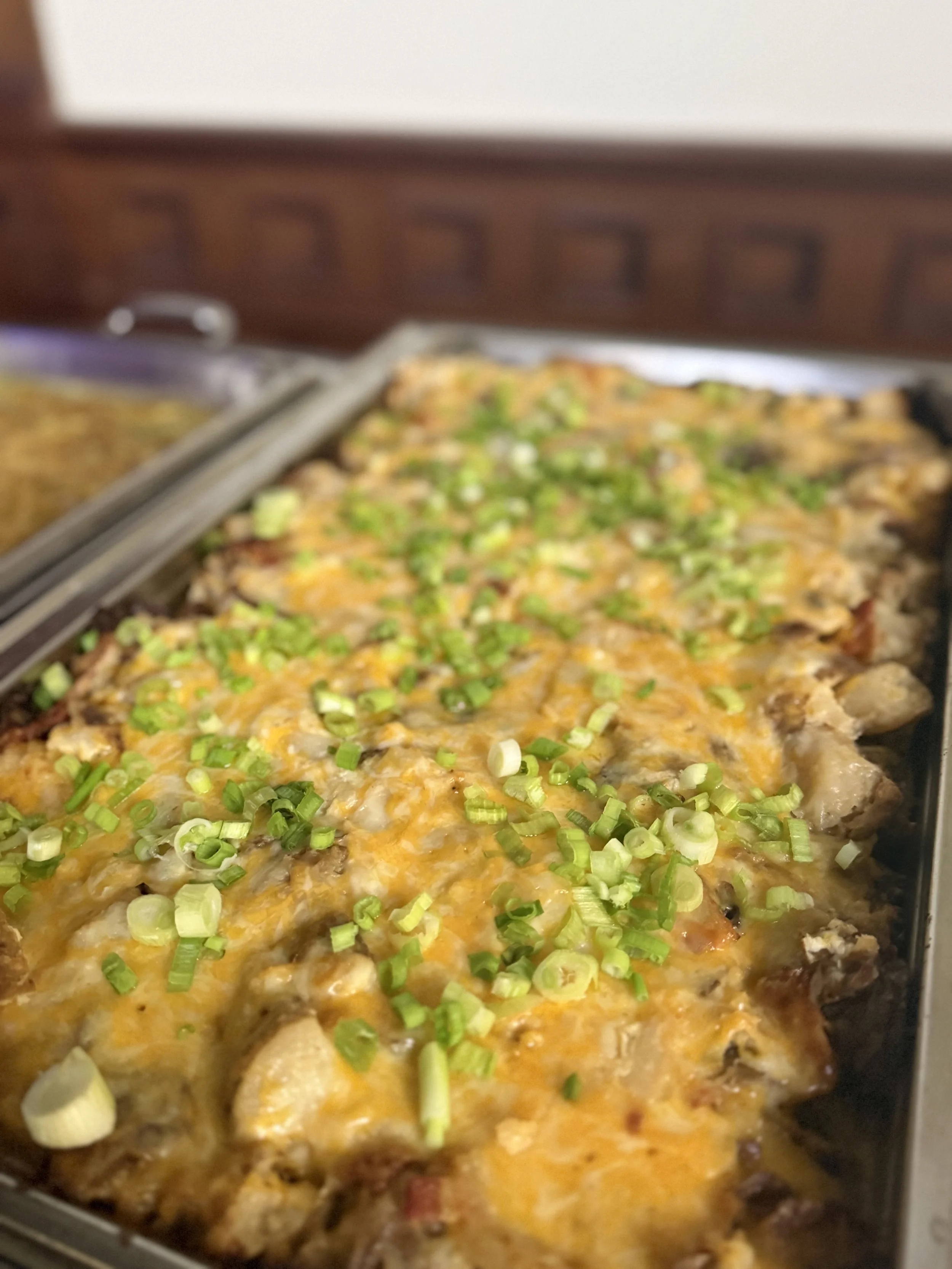 Baked cheesy casserole topped with chopped green onions in a metal serving dish.