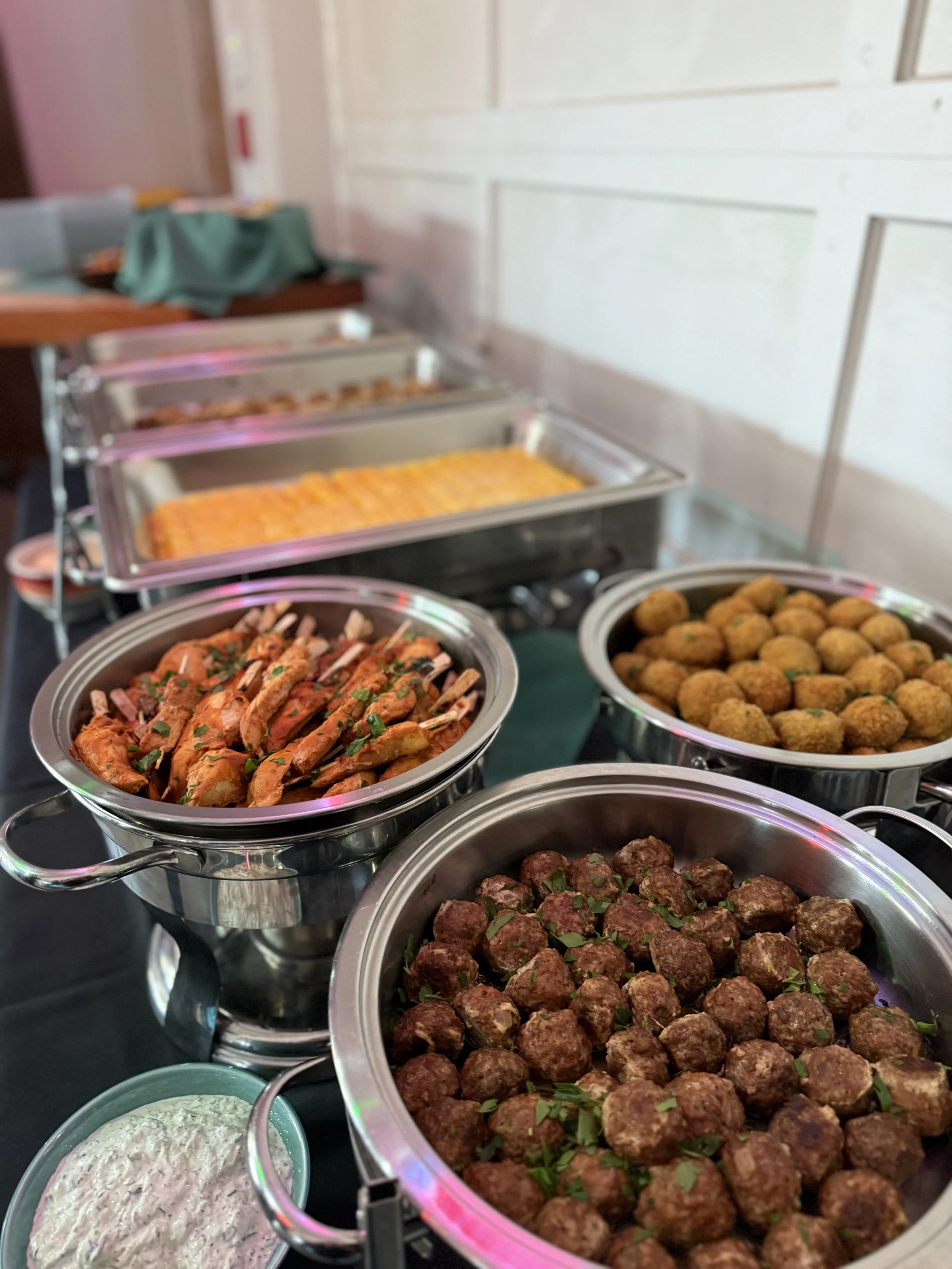 Buffet table with trays of meatballs, chicken wings, fried balls, and mashed potatoes.