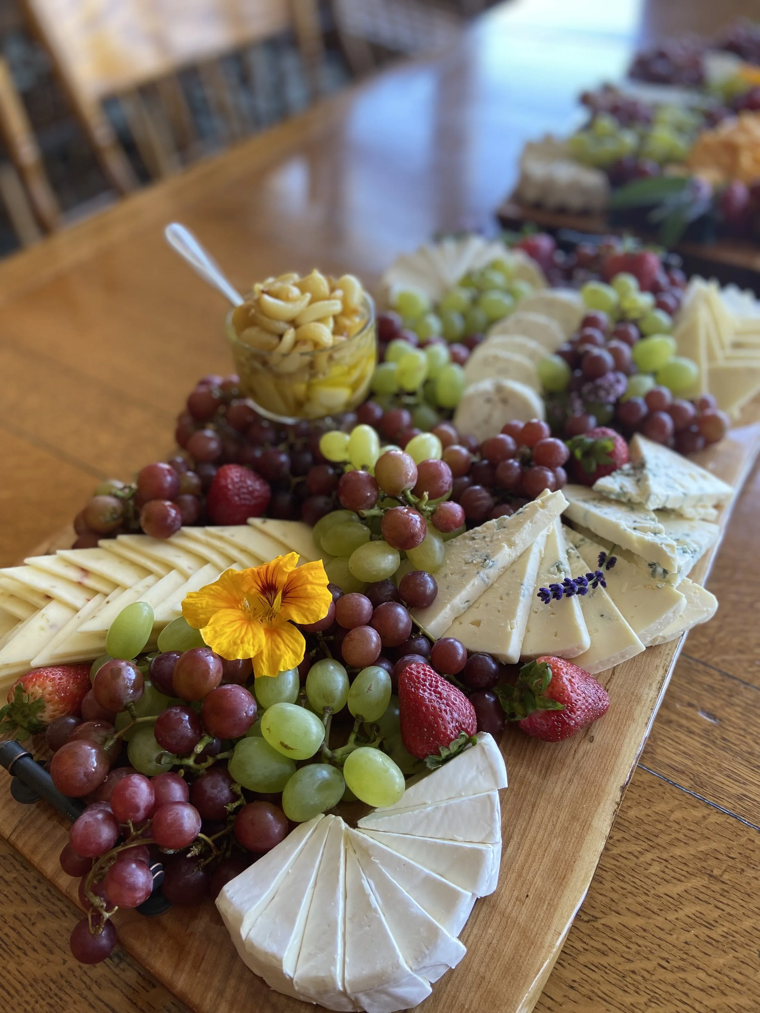 Cheese and fruit platter featuring sliced cheese, grapes, strawberries, and edible flowers on a wooden serving board.