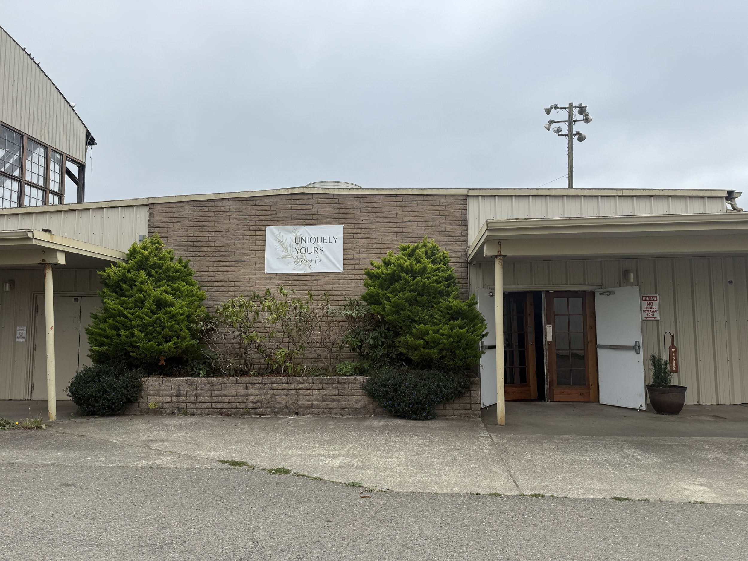 Exterior of a building with a sign that reads 'Uniquely Yours' and some green bushes in front.
