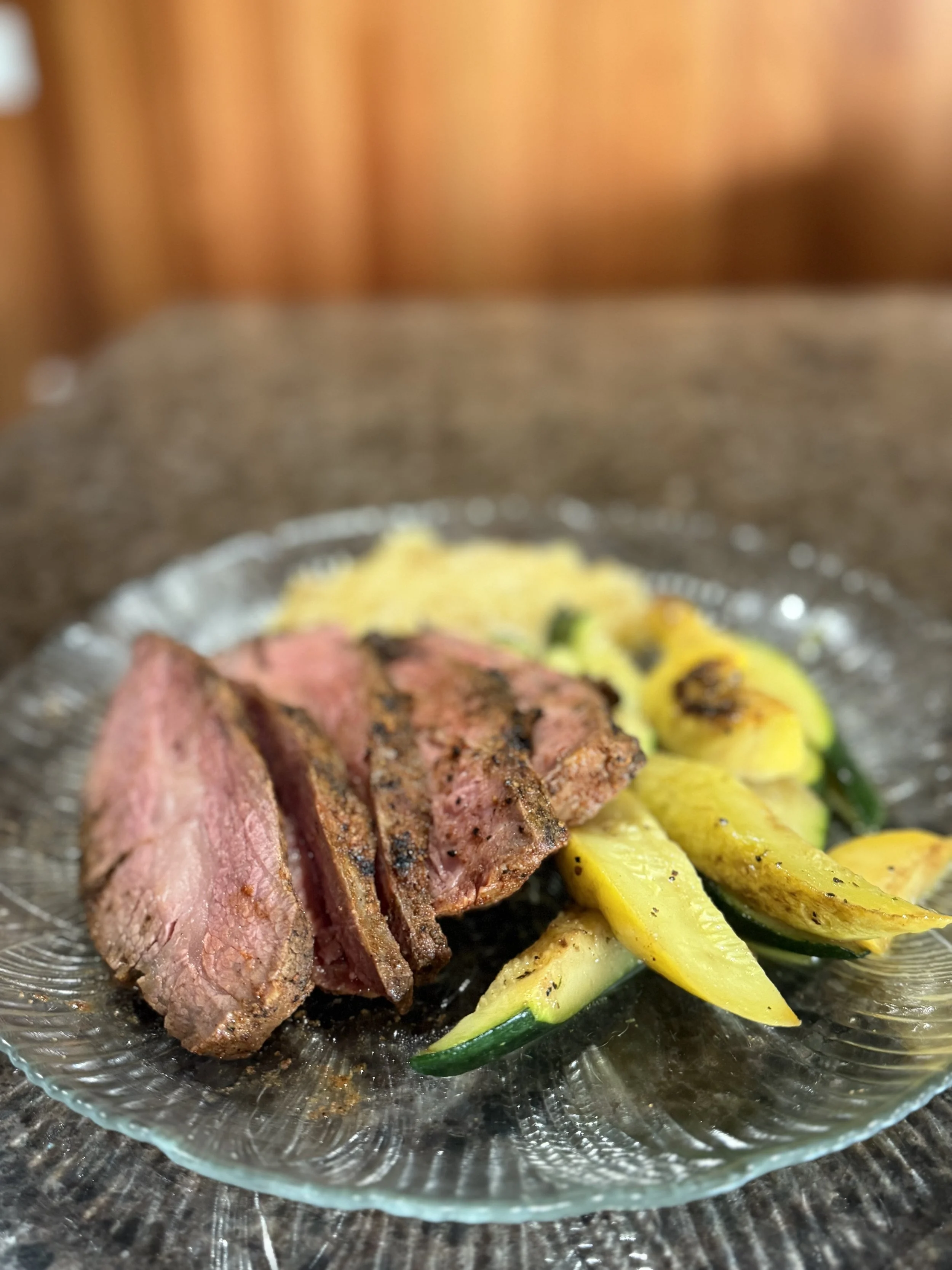 Cooked steak sliced and served with grilled yellow squash on a glass plate.