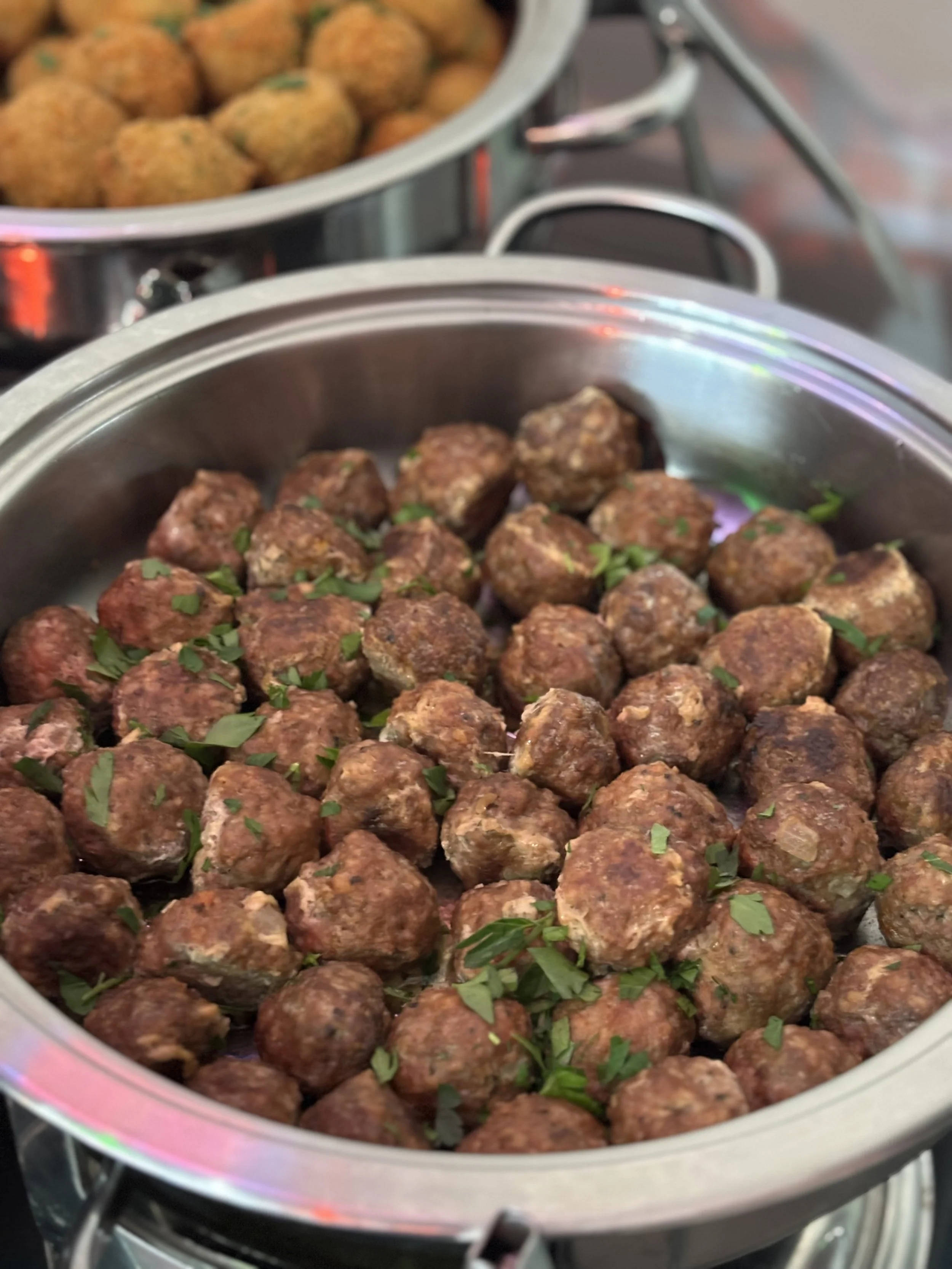 Close-up of a stainless steel chafing dish filled with cooked meatballs garnished with chopped parsley.