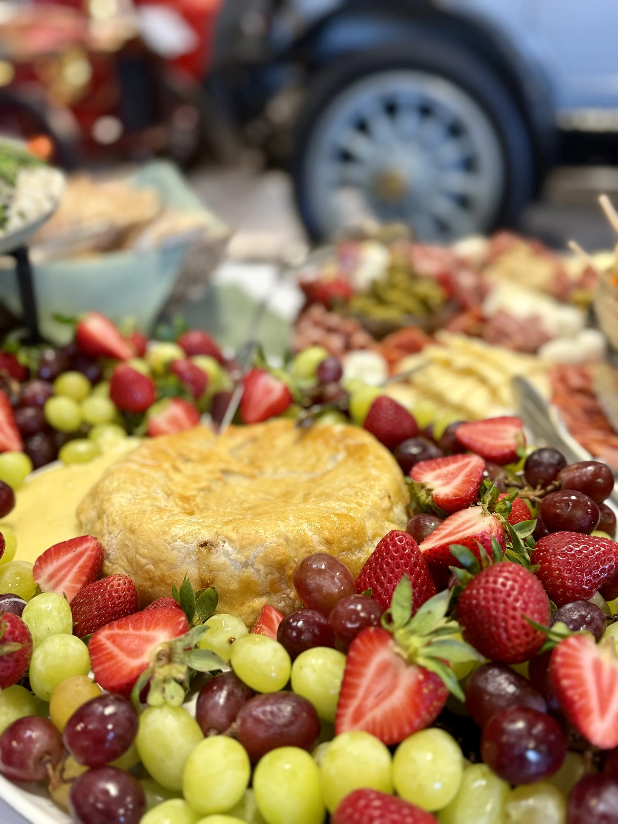 Fresh strawberries, green and red grapes surrounding a golden flaky pastry on a table at an outdoor market.
