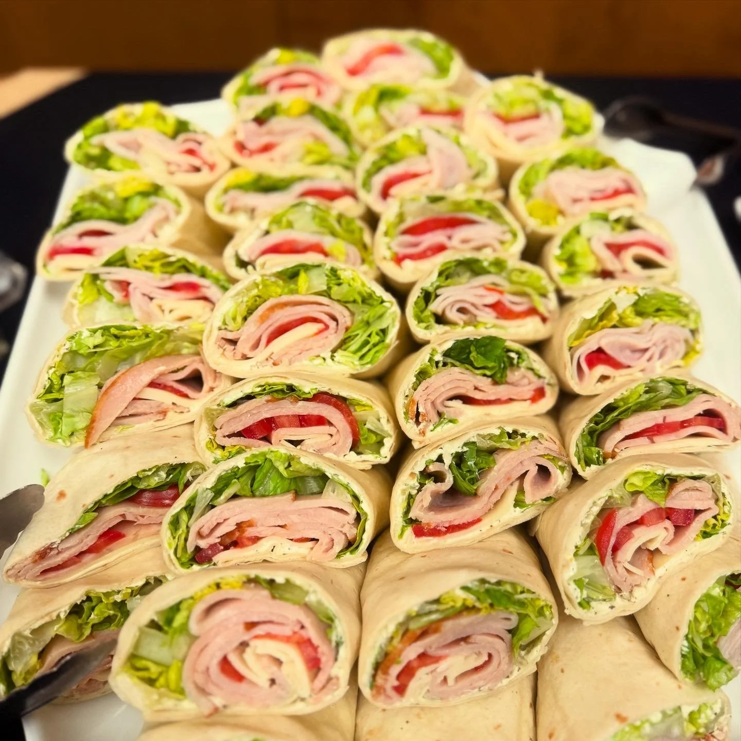 A platter of sliced wraps filled with lettuce, turkey, cheese, and tomatoes.