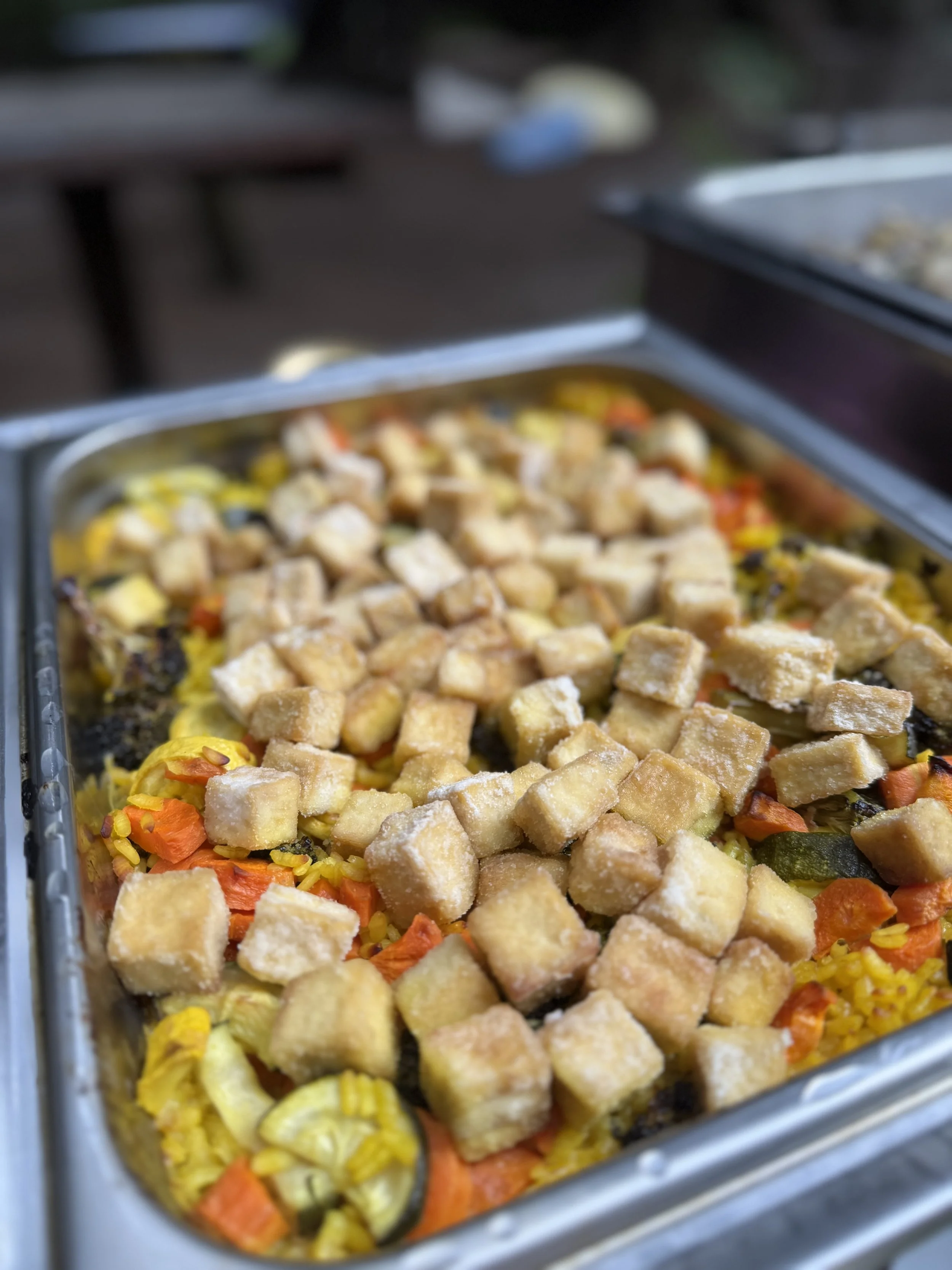 Tray of cooked chicken, mixed vegetables, and croutons in a buffet-style setting.