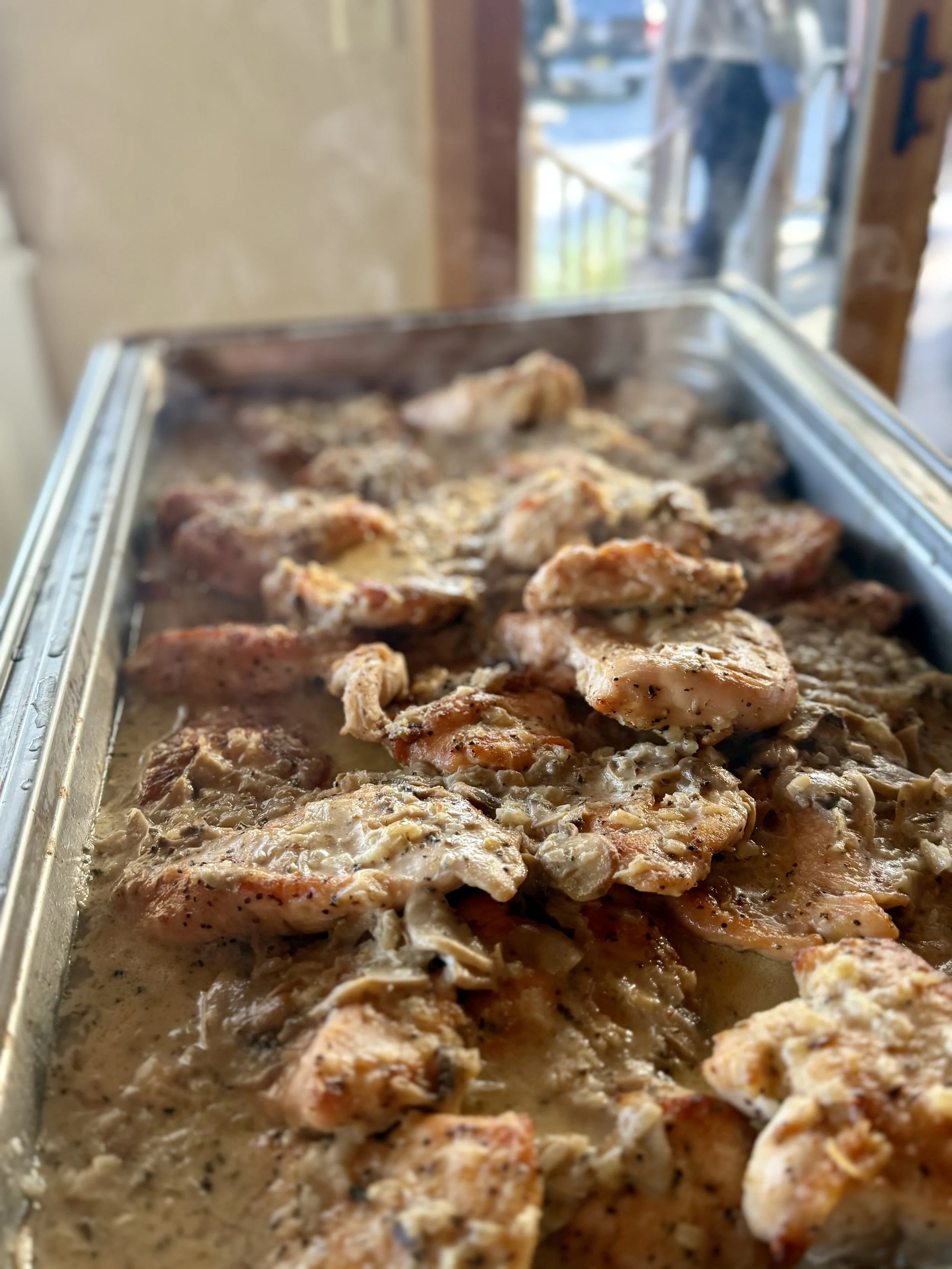 Hot cooked chicken with mushroom gravy in a stainless steel pan on a buffet table.