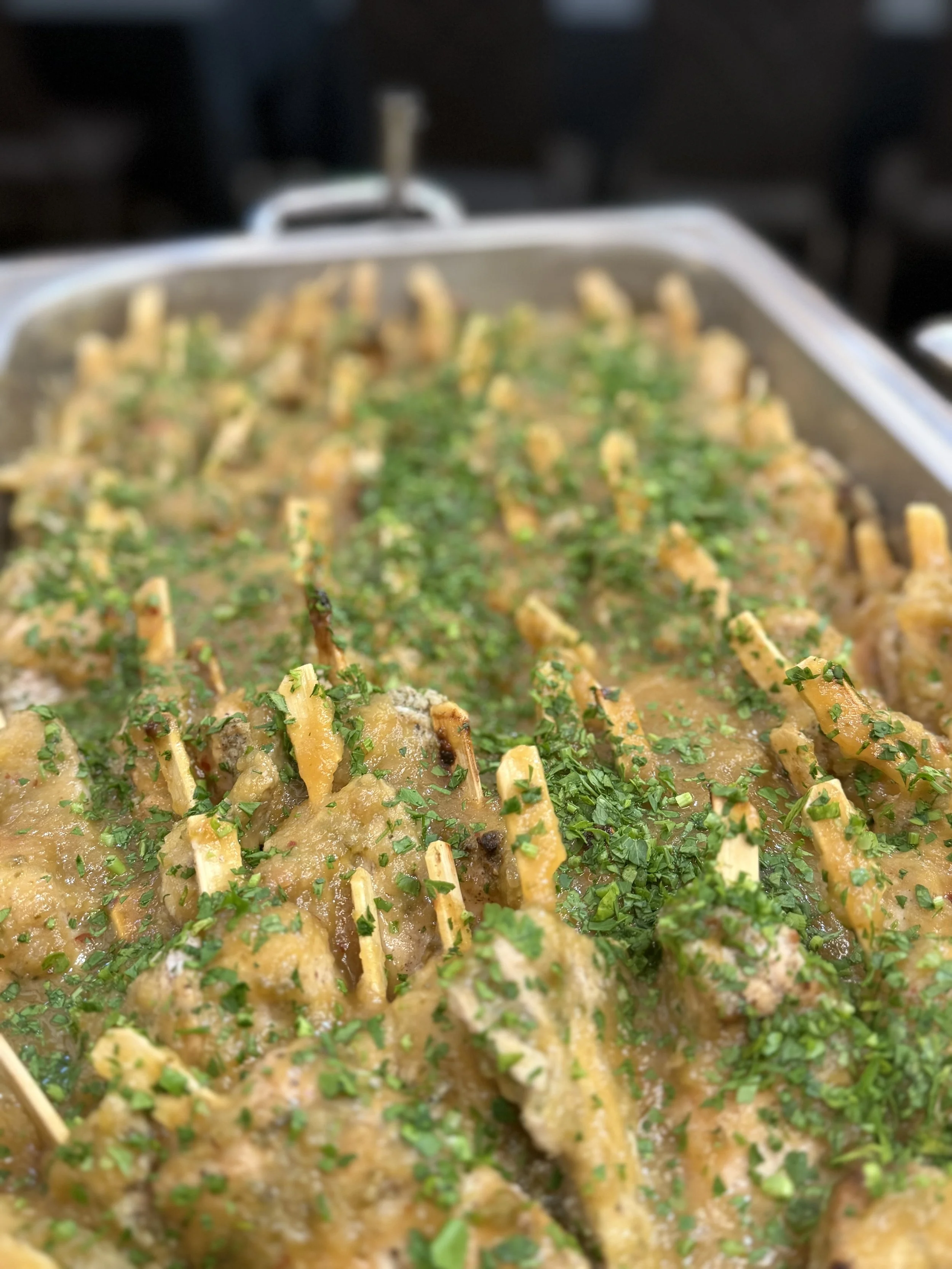 A large baking dish filled with cooked chicken enchiladas covered in sauce and garnished with chopped parsley.