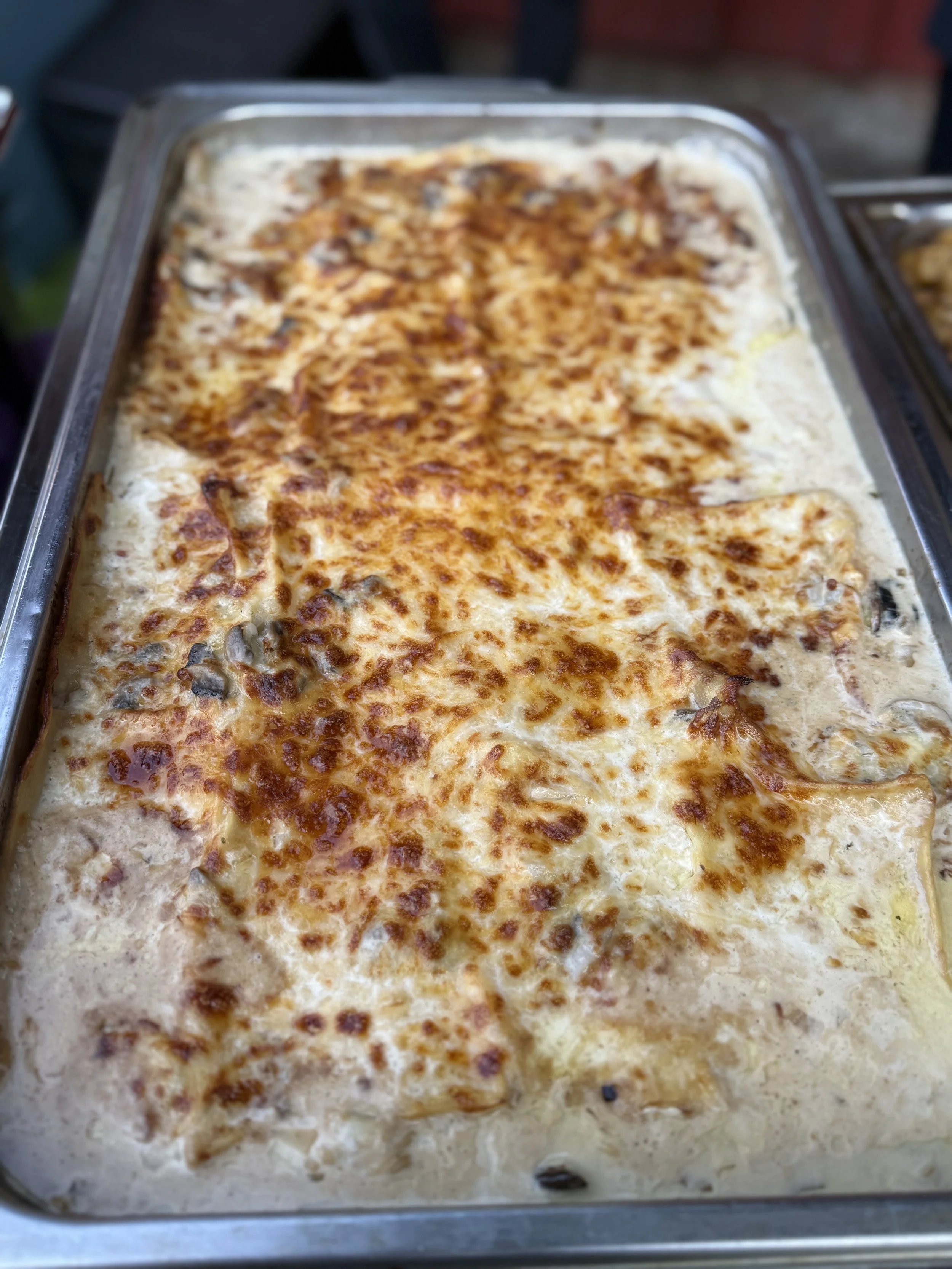 Baked dish with melted cheese and browned toppings in a large metal tray.