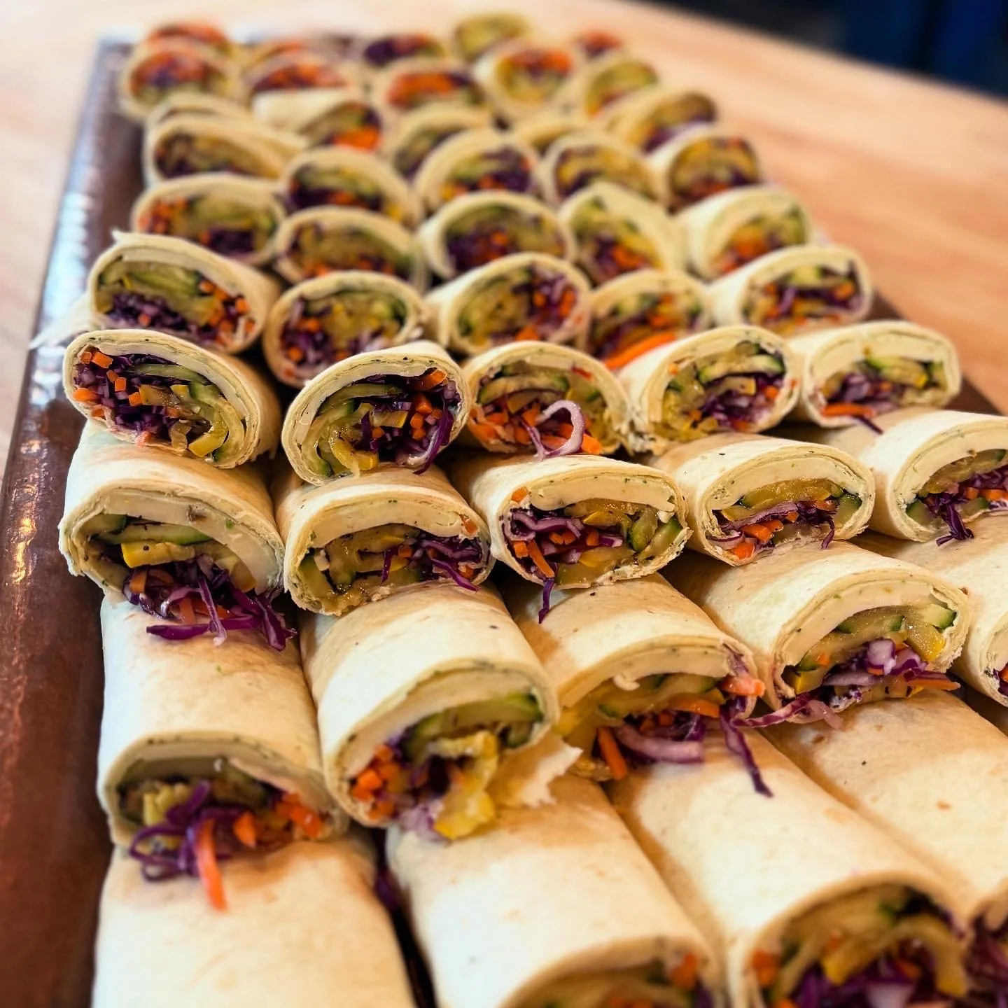 Rows of cut vegetable wraps filled with shredded purple cabbage, orange carrots, and green cucumbers on a large wooden serving platter.