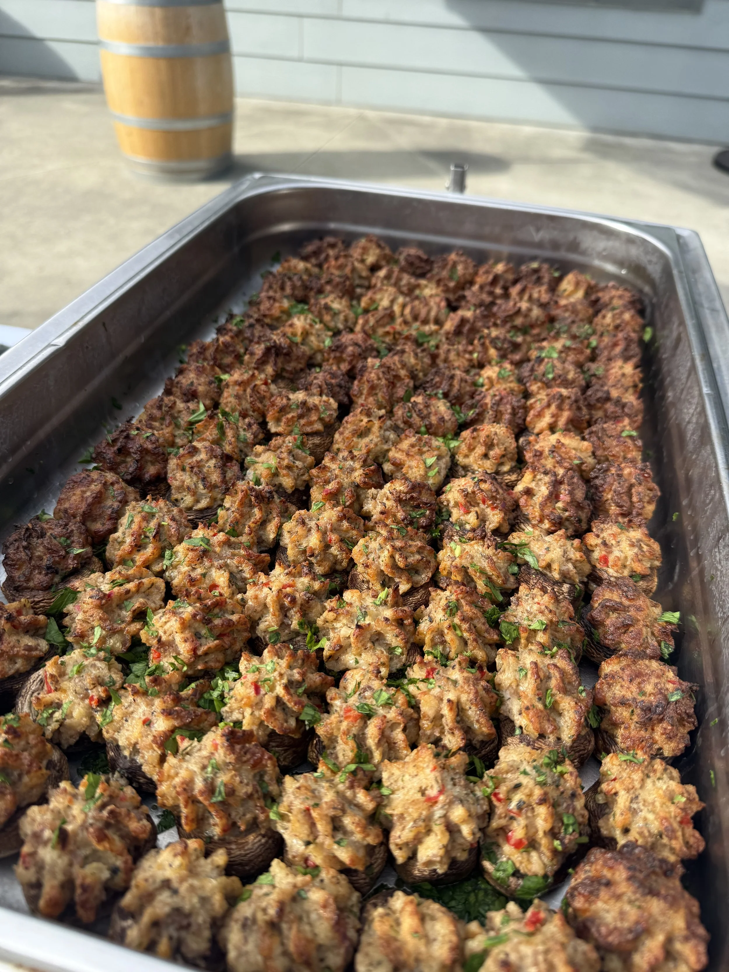 A metal tray filled with cooked meatballs garnished with chopped parsley, set on a table outdoors.