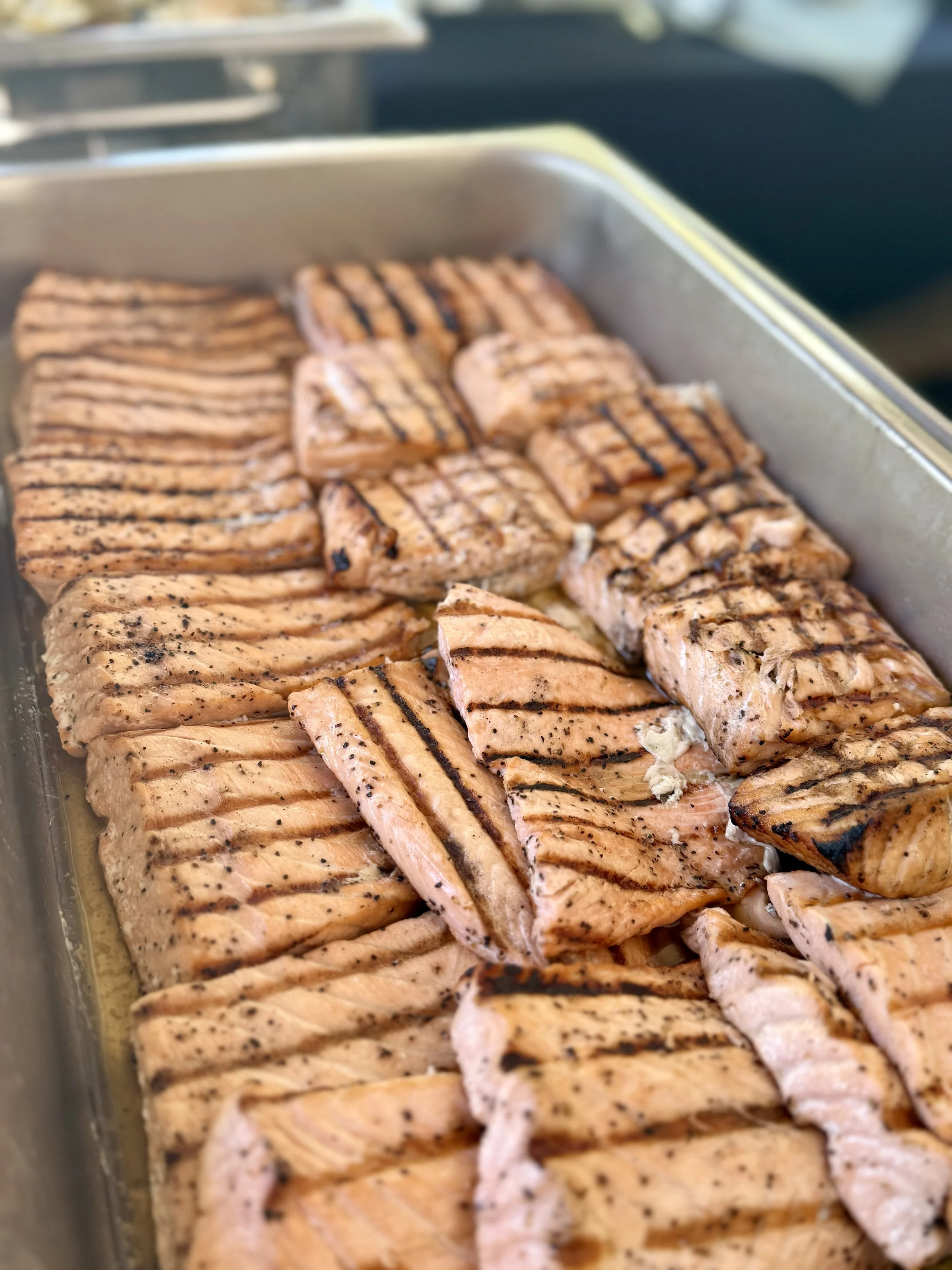 Grilled salmon fillets in a metal tray, each with grill marks and seasoning.