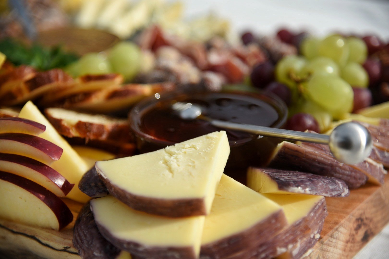 Close-up of a cheese and fruit platter with sliced cheese, grapes, and a bowl of dark sauce.