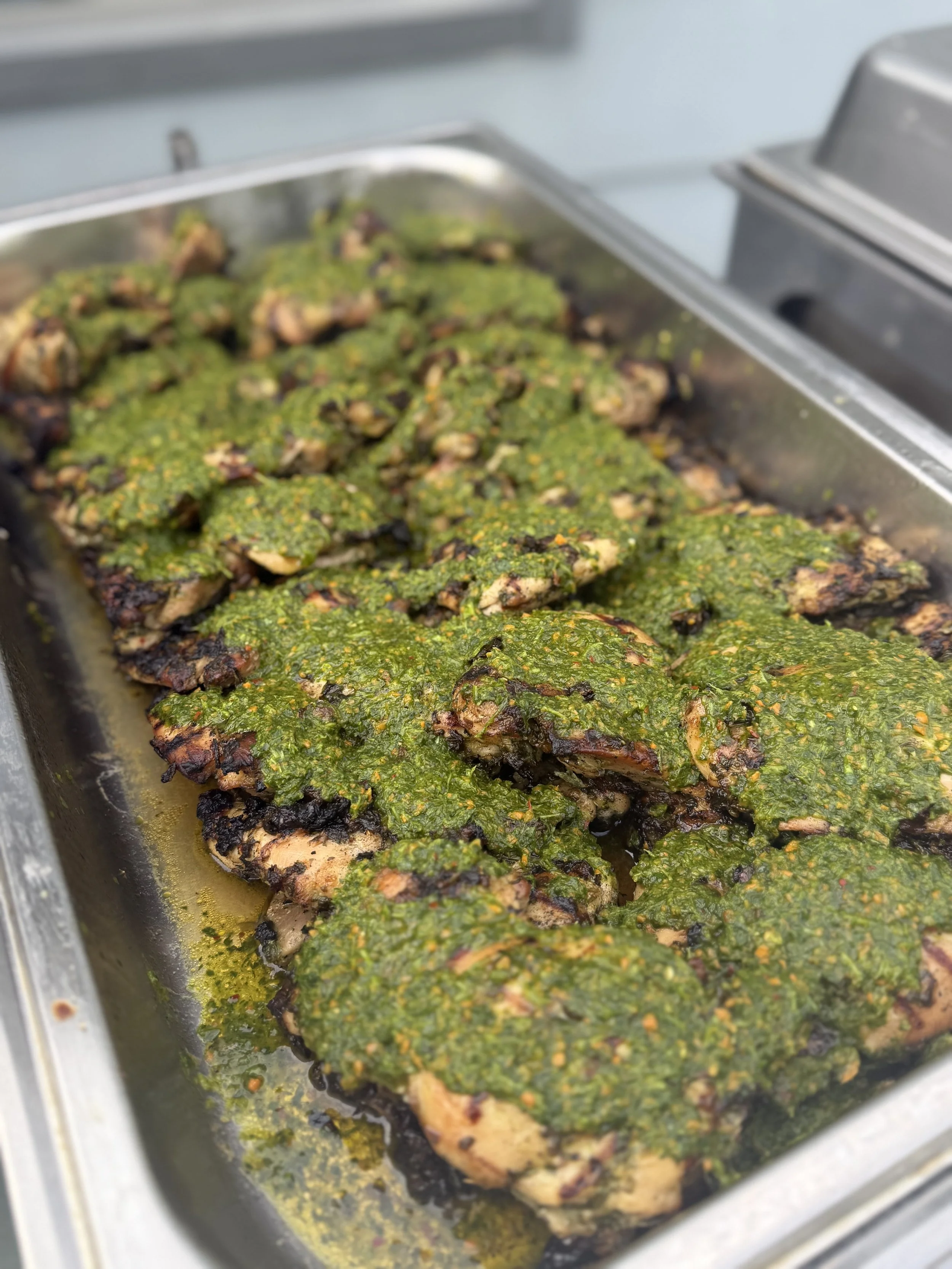 Tray of grilled chicken pieces topped with green herb sauce.