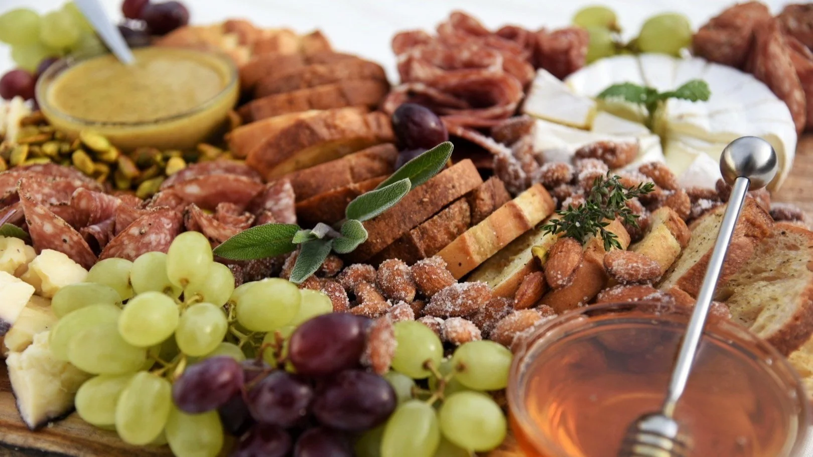 Charcuterie board with grapes, cheese, nuts, crackers, and honey.