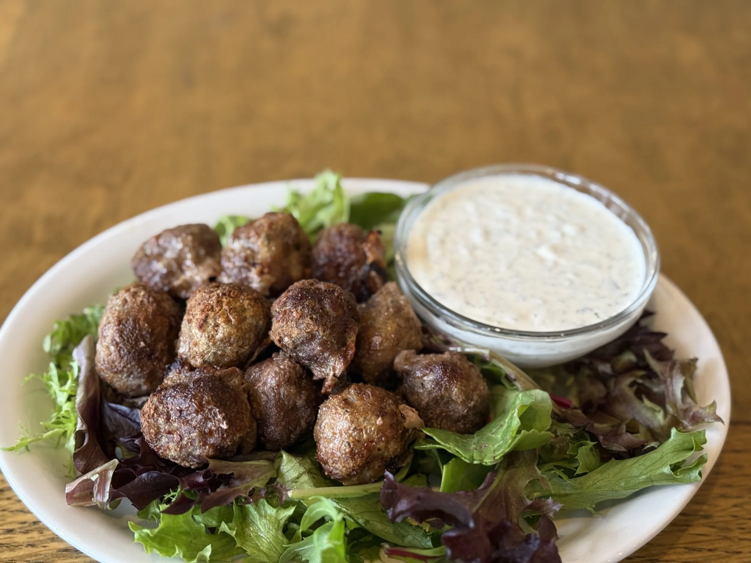 Plate of meatballs with salad greens and a bowl of ranch dressing on a wooden table.