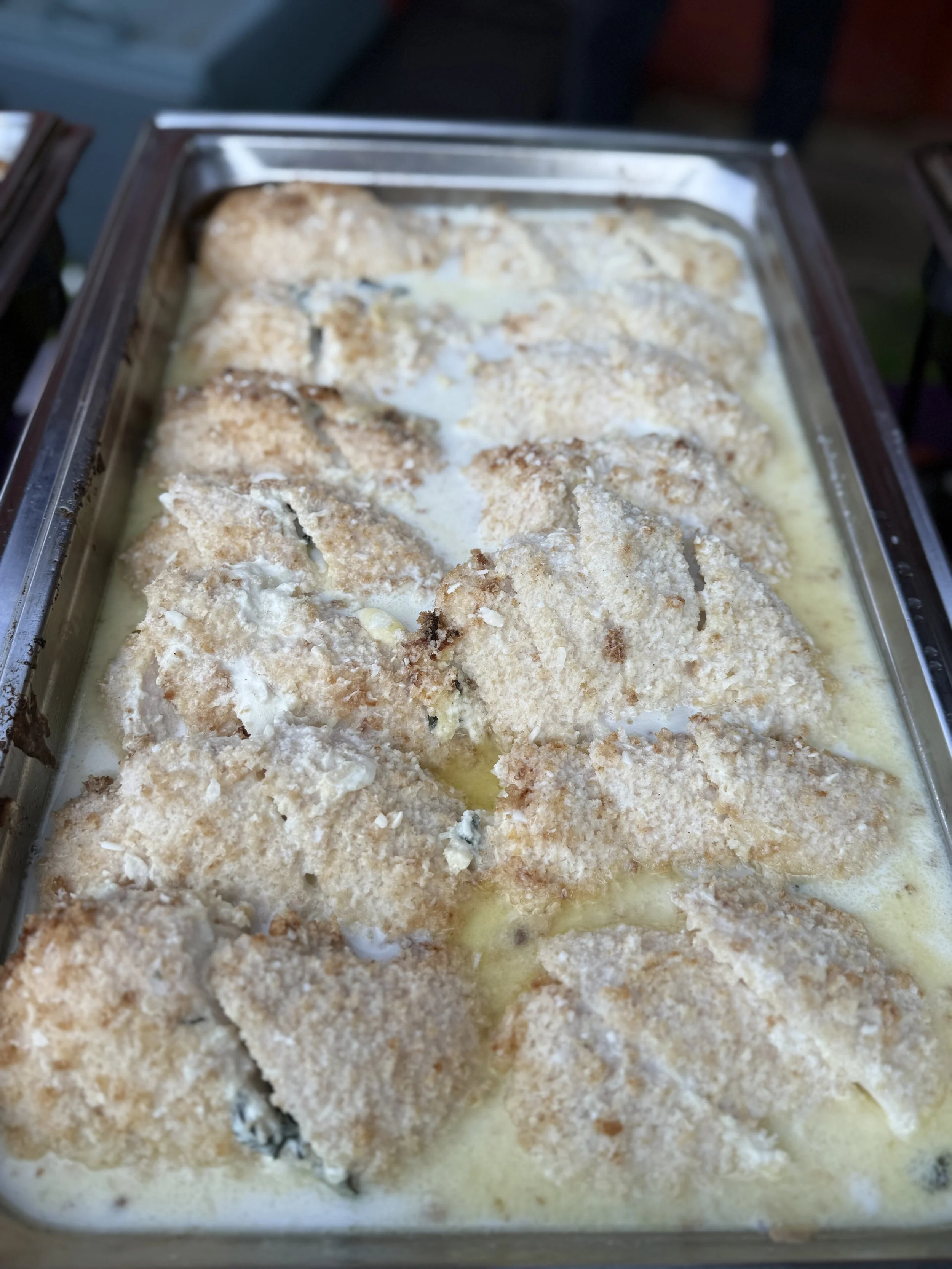 Baked chicken roulade stuffed with butternut squash, chevres and caramelized onions in a metal tray, topped with a creamy pesto sauce.