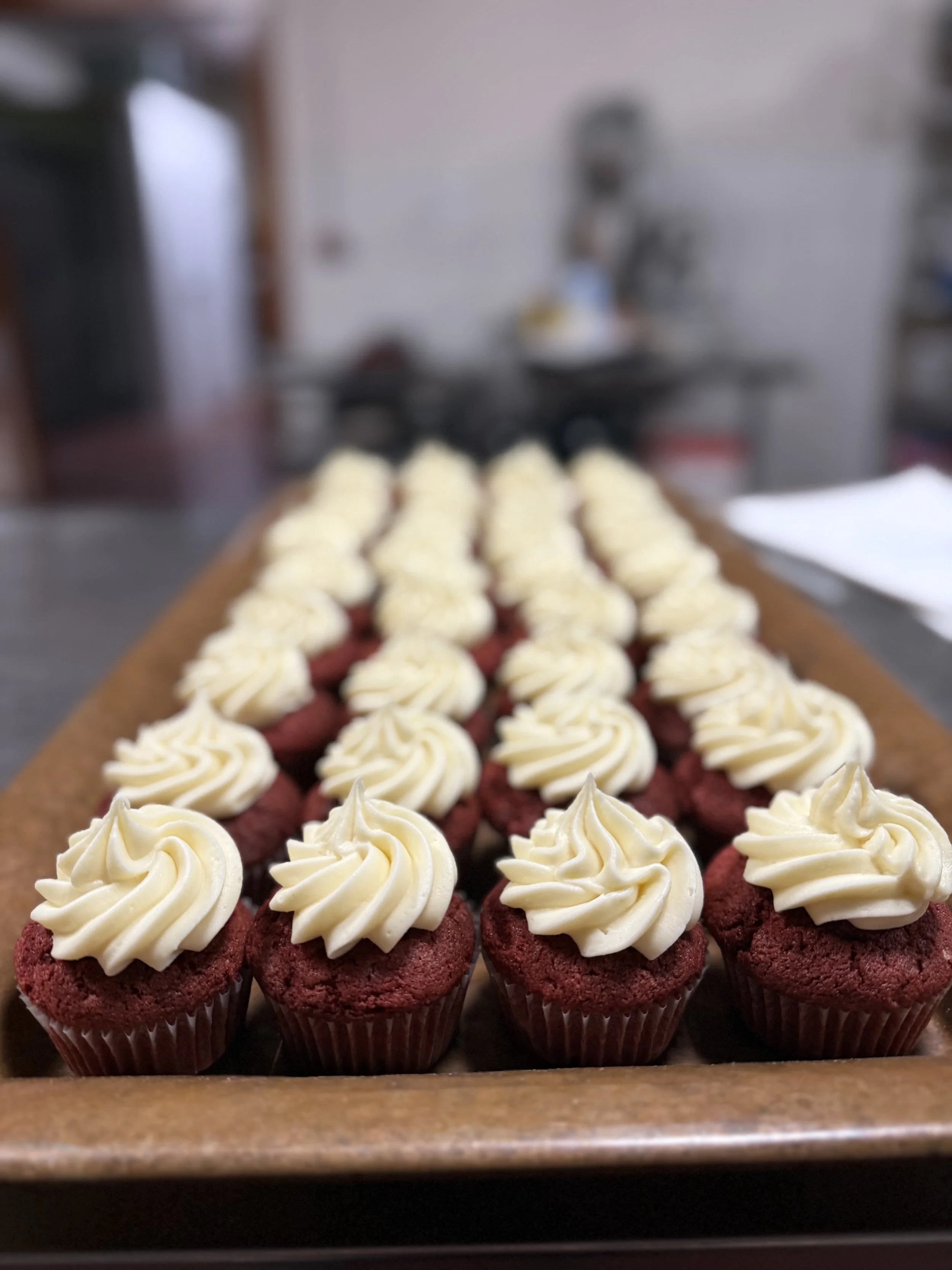Red velvet cupcakes with white frosting arranged on a wooden tray.
