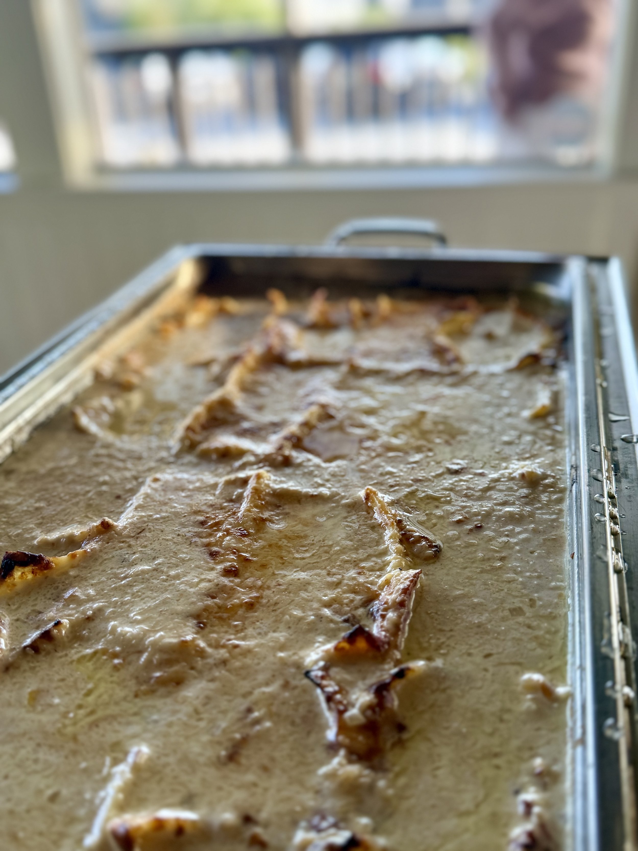 A tray of raw bacon cooking in a creamy sauce, on a metal baking sheet in front of a window.
