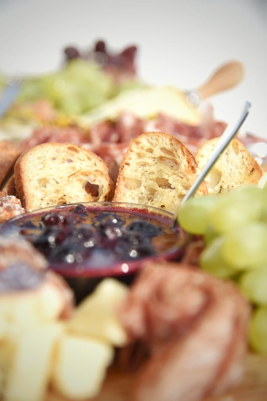 Close-up of a cheese, bread, and fruit platter, with slices of bread, black grape jelly, green grapes, and cheese cubes.