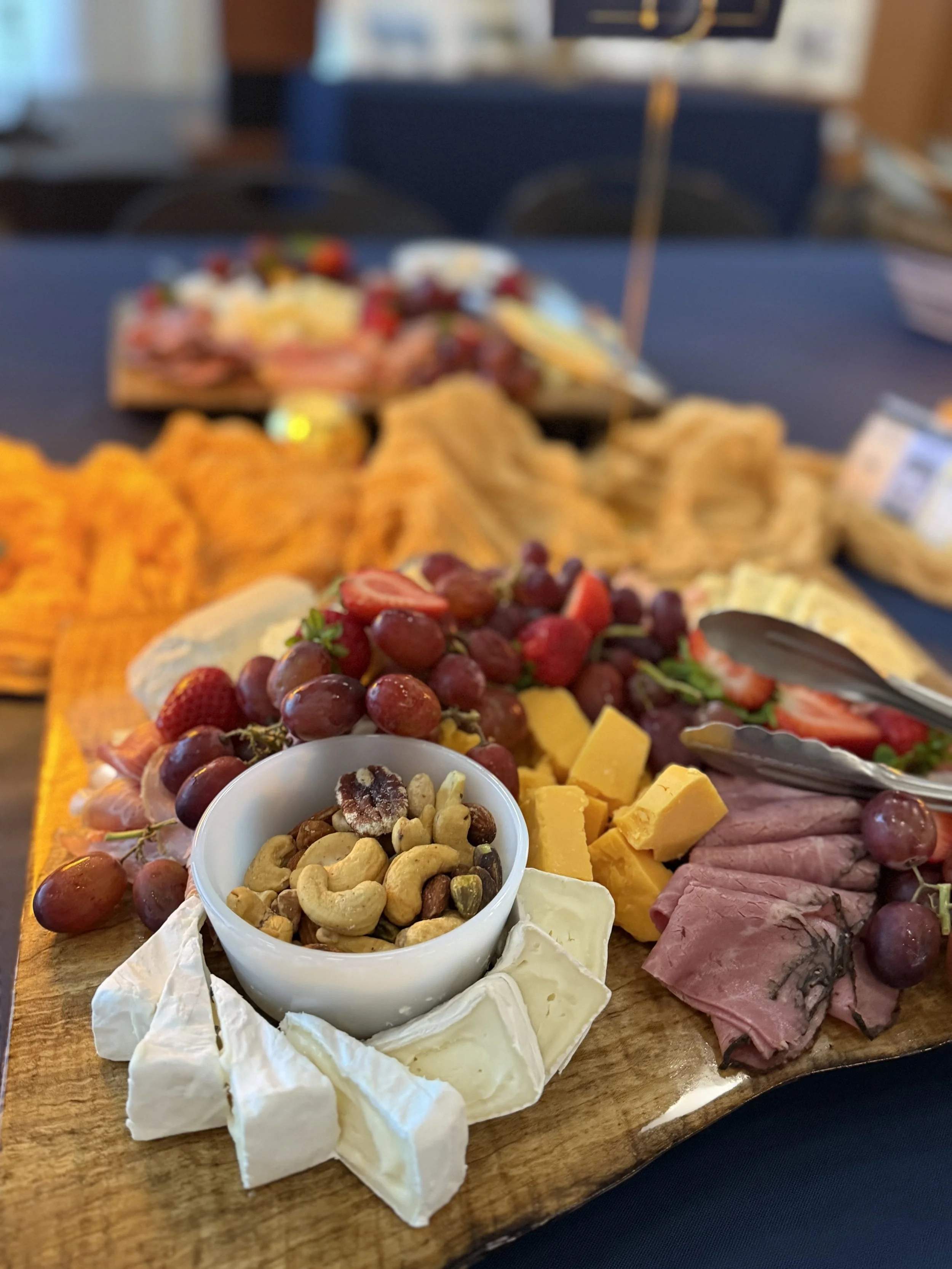 Cheese and fruit platter with grapes, strawberries, cubed cheese, sliced meat, and mixed nuts on a wooden board.