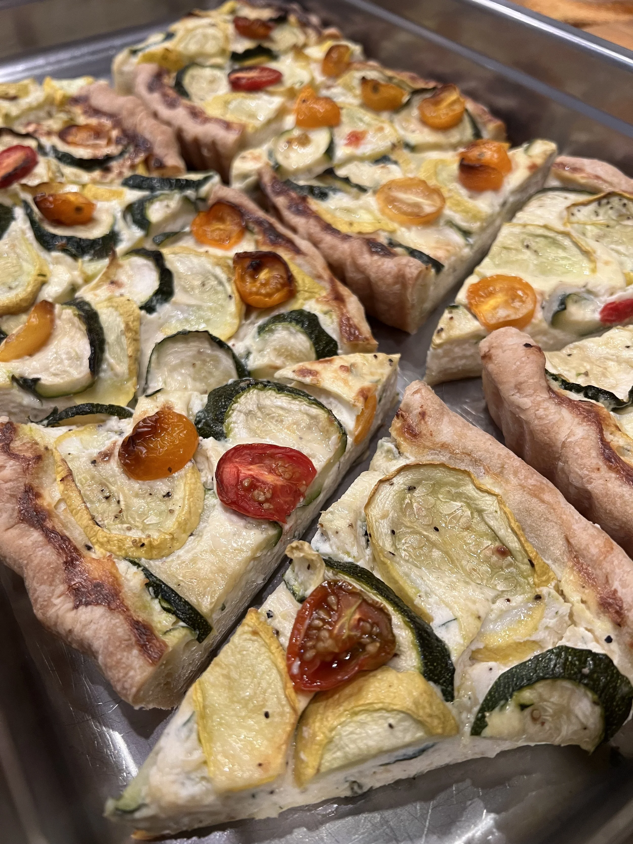 Slices of vegetable quiche with zucchini, cherry tomatoes, and yellow squash on a baking tray.