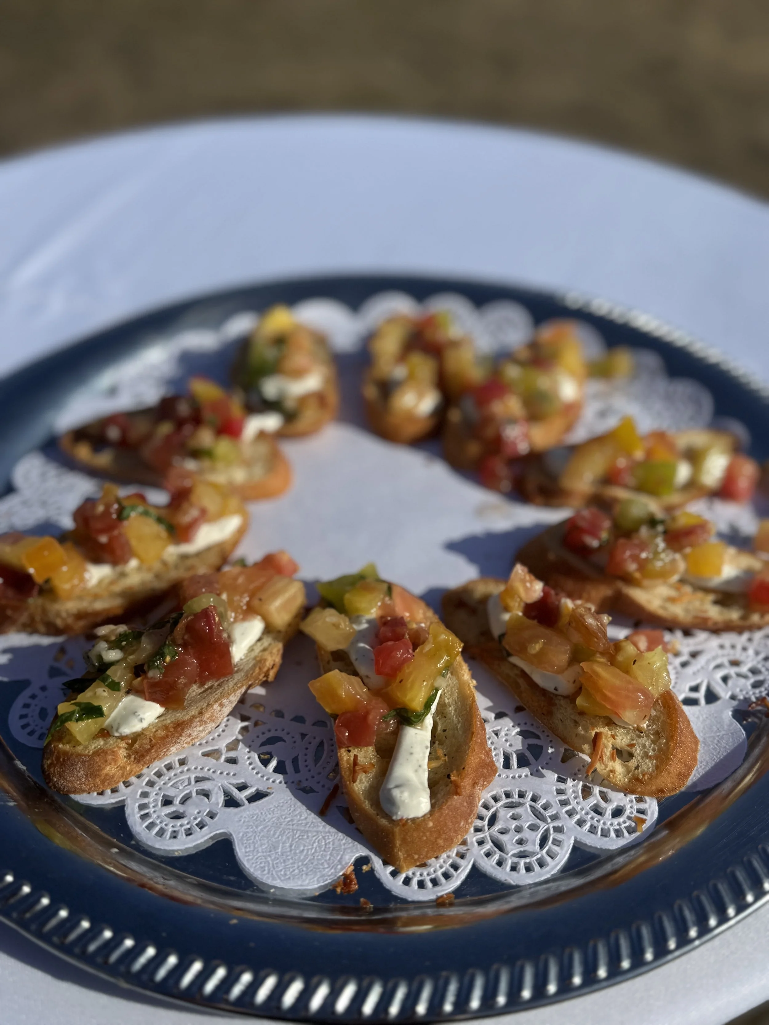 Tray of toasted baguette slices topped with chopped vegetables and cream cheese for appetizers, arranged on a decorative paper doily.