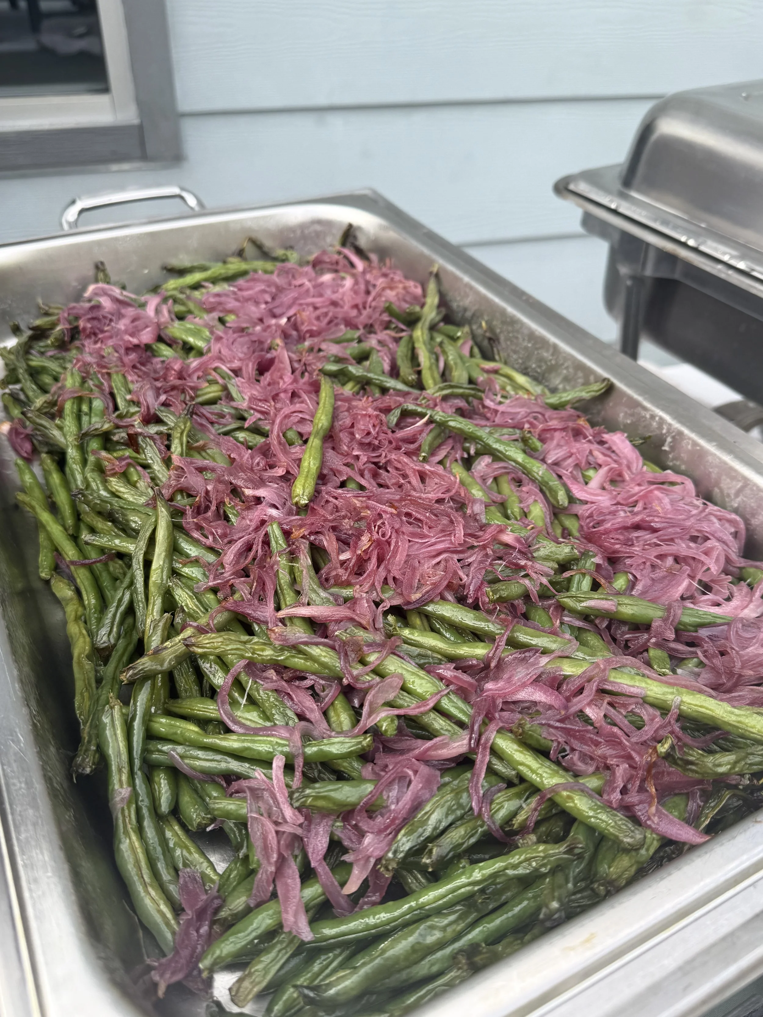 A stainless steel tray filled with cooked green beans topped with pickled red onions.