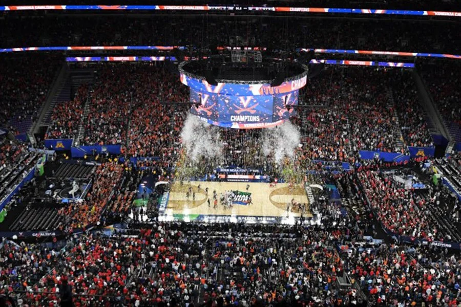 Crowd celebrating in a basketball arena with confetti falling after a game victory, scoreboard displays 'CHAMPIONS'