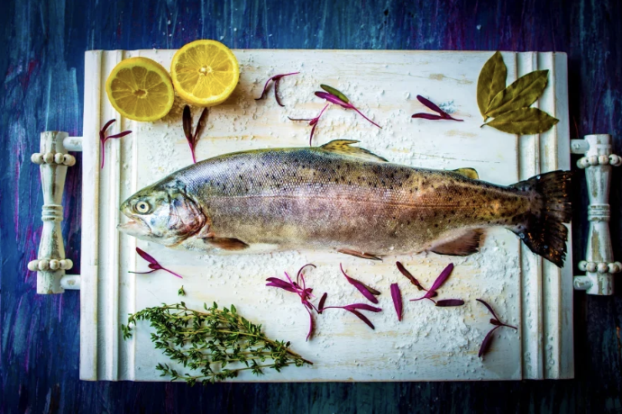 Freshly caught fish on a white cutting board with lemon slices, herbs, and garnishes.