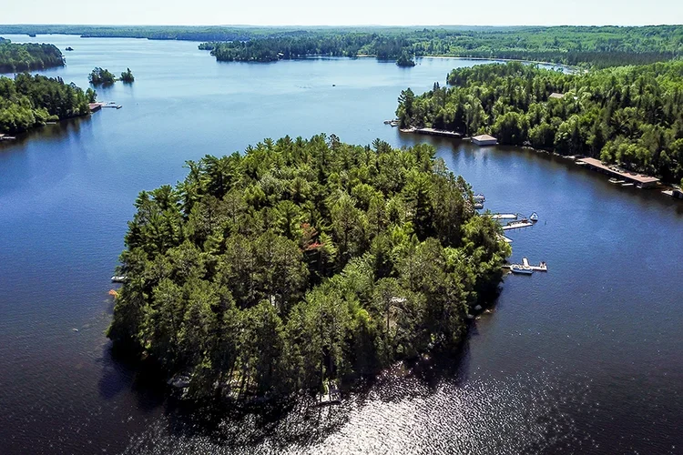 Aerial view of a small forested island in a large lake with boats docked along the shoreline, surrounded by other wooded islands and water.